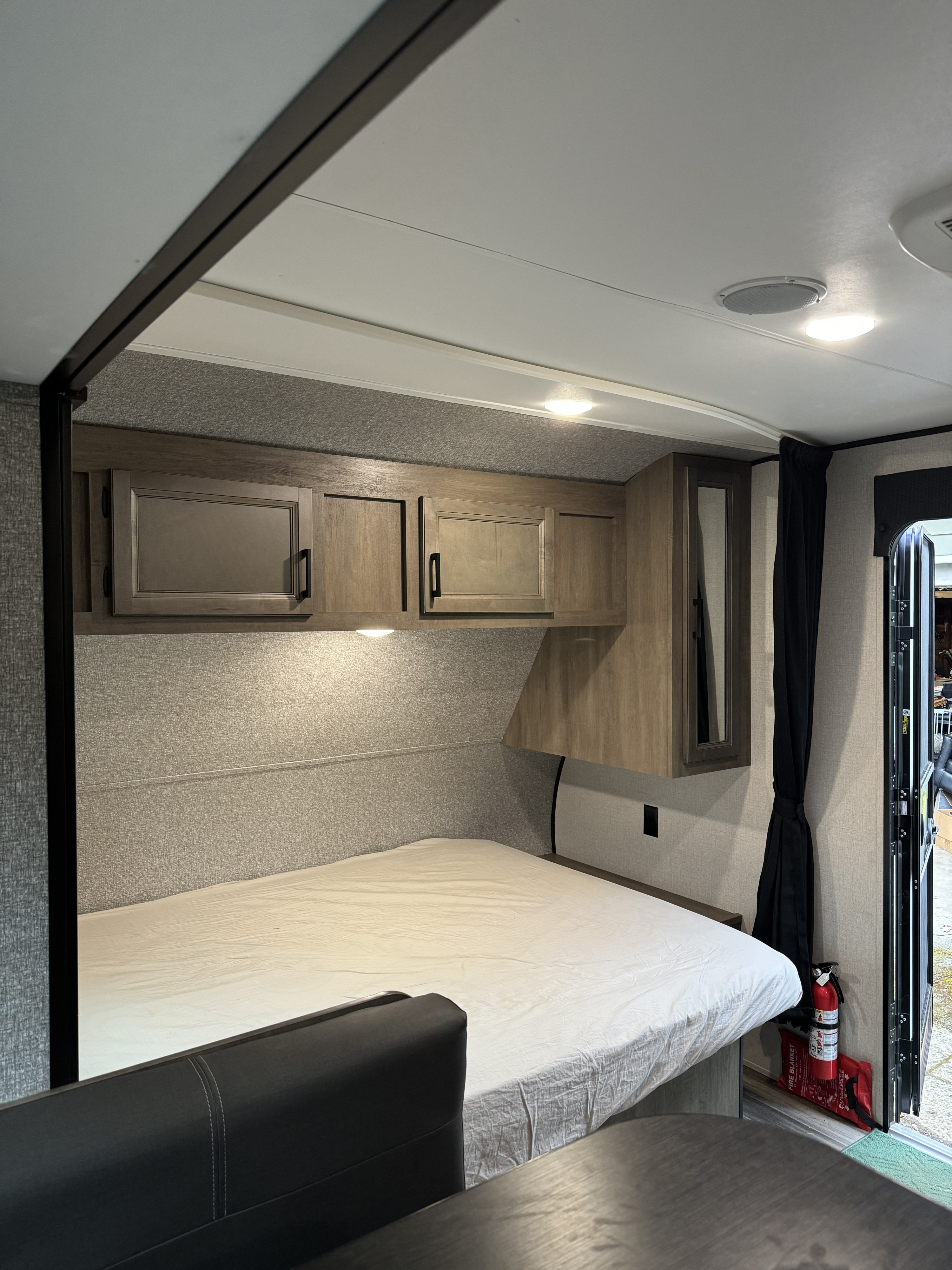 Inside a well-equipped RV rental, showing the bed, overhead cabinets, and essential fire safety gear by the open door.. Jayco StarCraft 2022