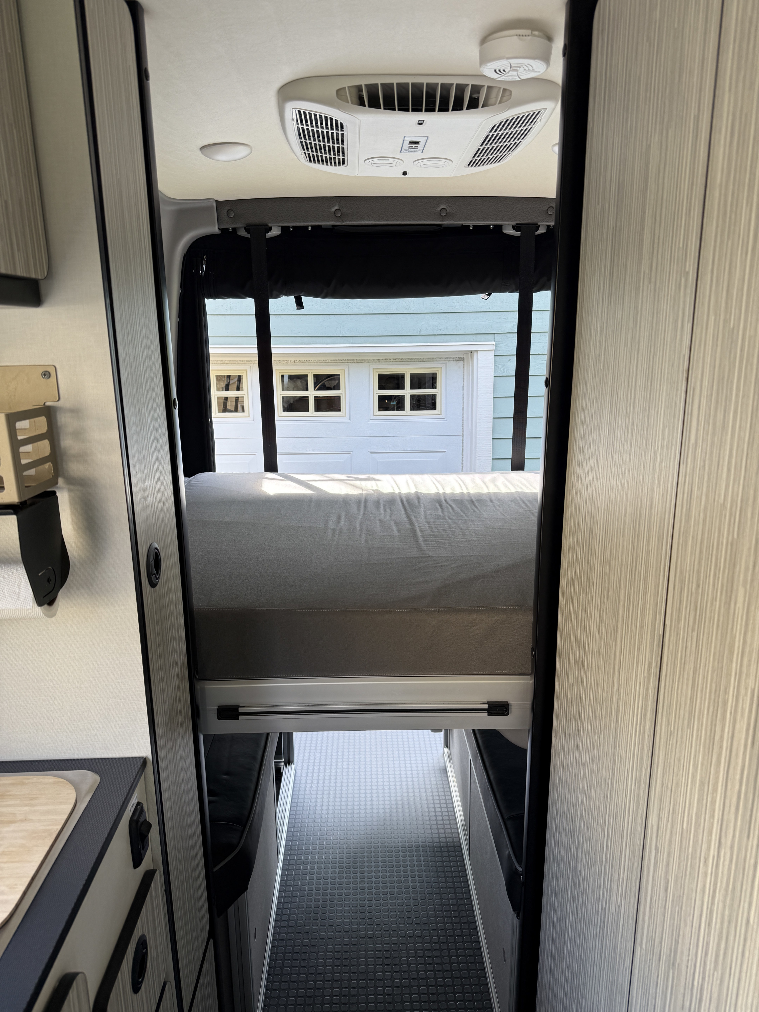 This RV rental features a raised bed over a hallway with benches, a small kitchen, and overhead AC unit.. Winnebago Revel 2022