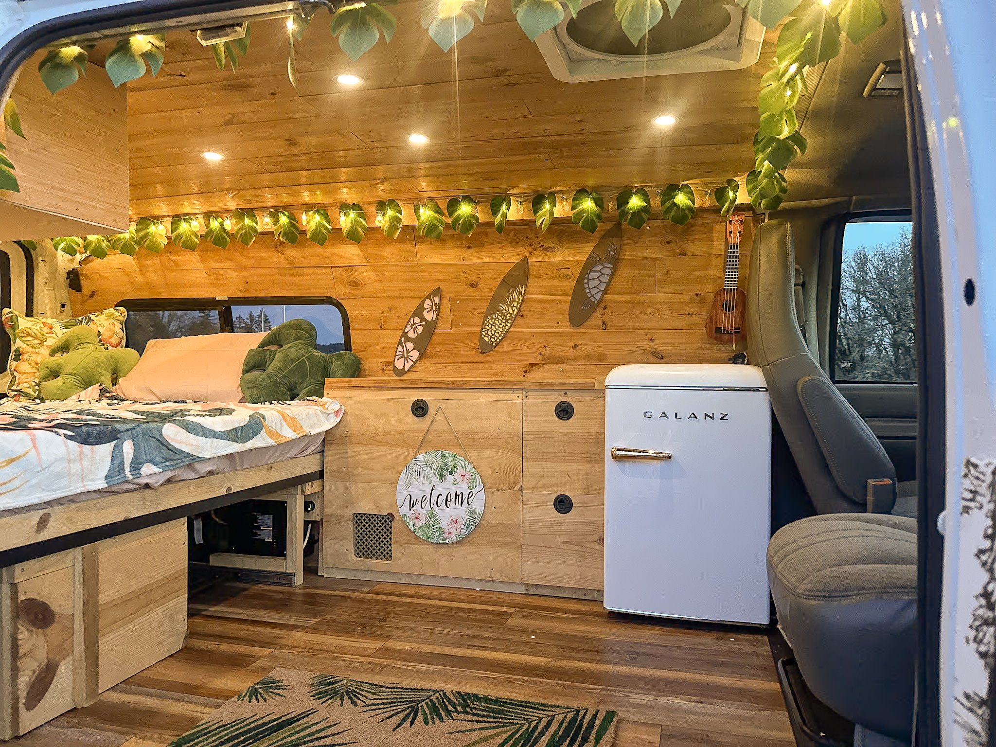 Cozy RV rental interior with wooden walls, bed, string lights, mini-fridge, and ukulele. Perfect for your next adventure.. Chevrolet Express 1999