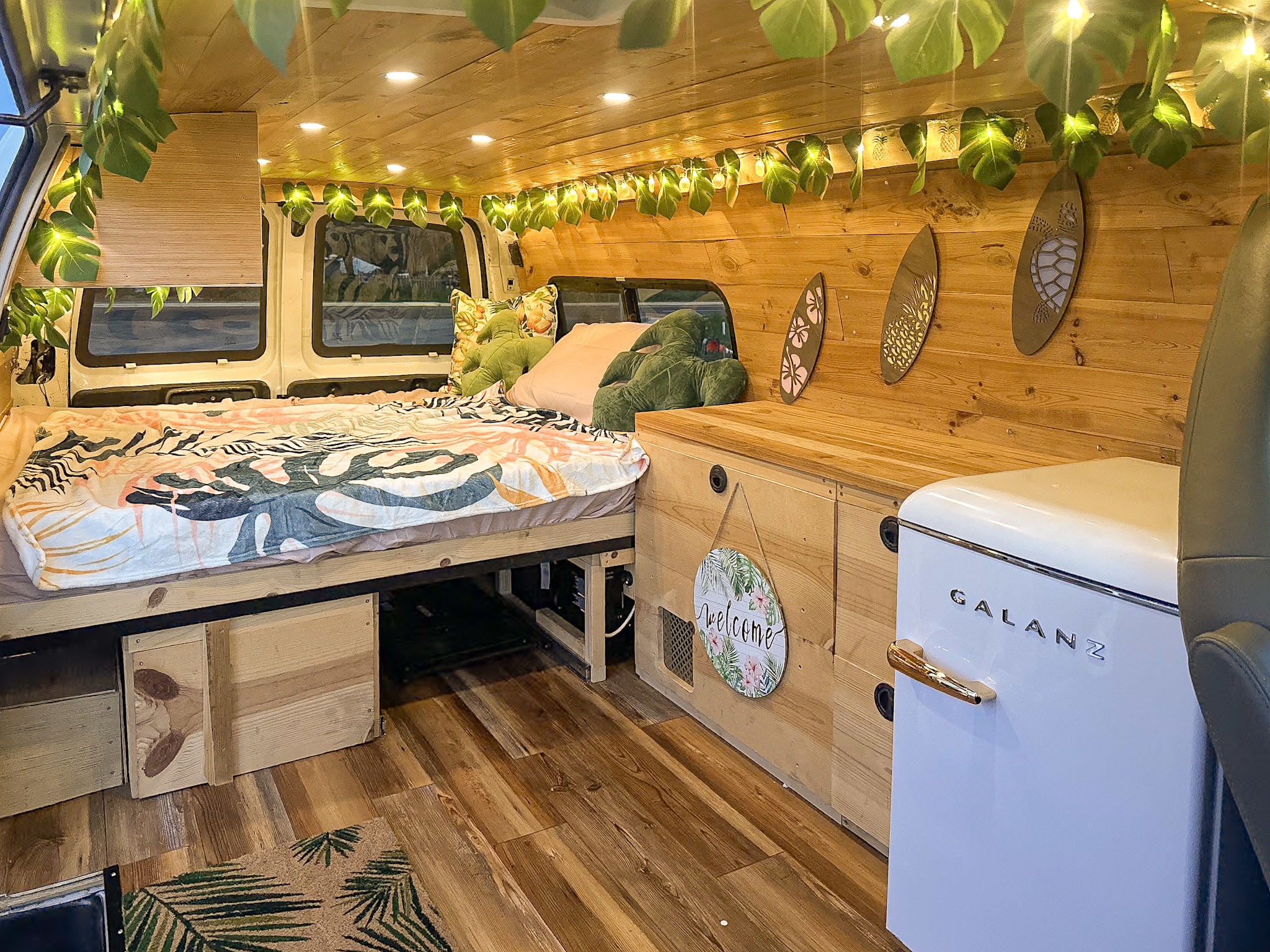 Tropical-themed RV rental interior with leaf lights, patterned bedding, wooden walls, and a retro fridge.. Chevrolet Express 1999