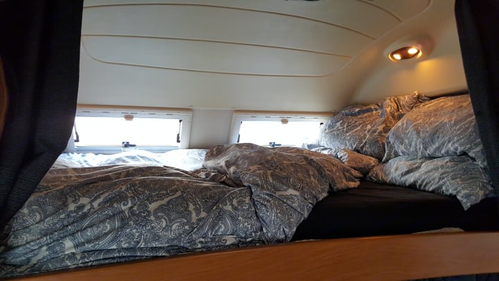 Comfortable RV rental sleeping area with cozy bed, patterned bedding, small windows, and overhead lights.. Iveco Laika Ecovip 9.1g 2003