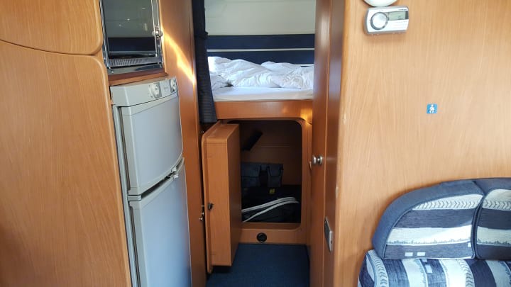 Inside an RV rental: view of bed over storage, compact kitchen (fridge, microwave), and seating area.. Iveco Laika Ecovip 9.1g 2003