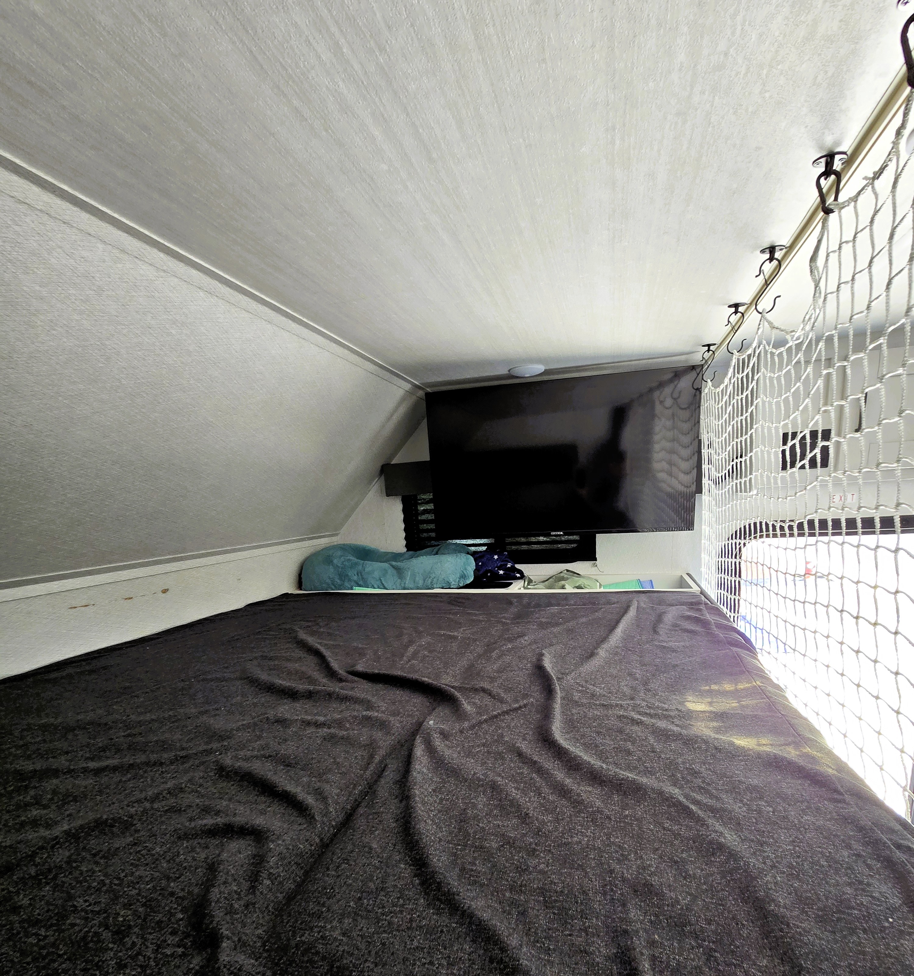 Experience our RV rental's comfortable bunk: dark bedding, mounted TV, and safety net for secure rest.. East to west Entrada 2025