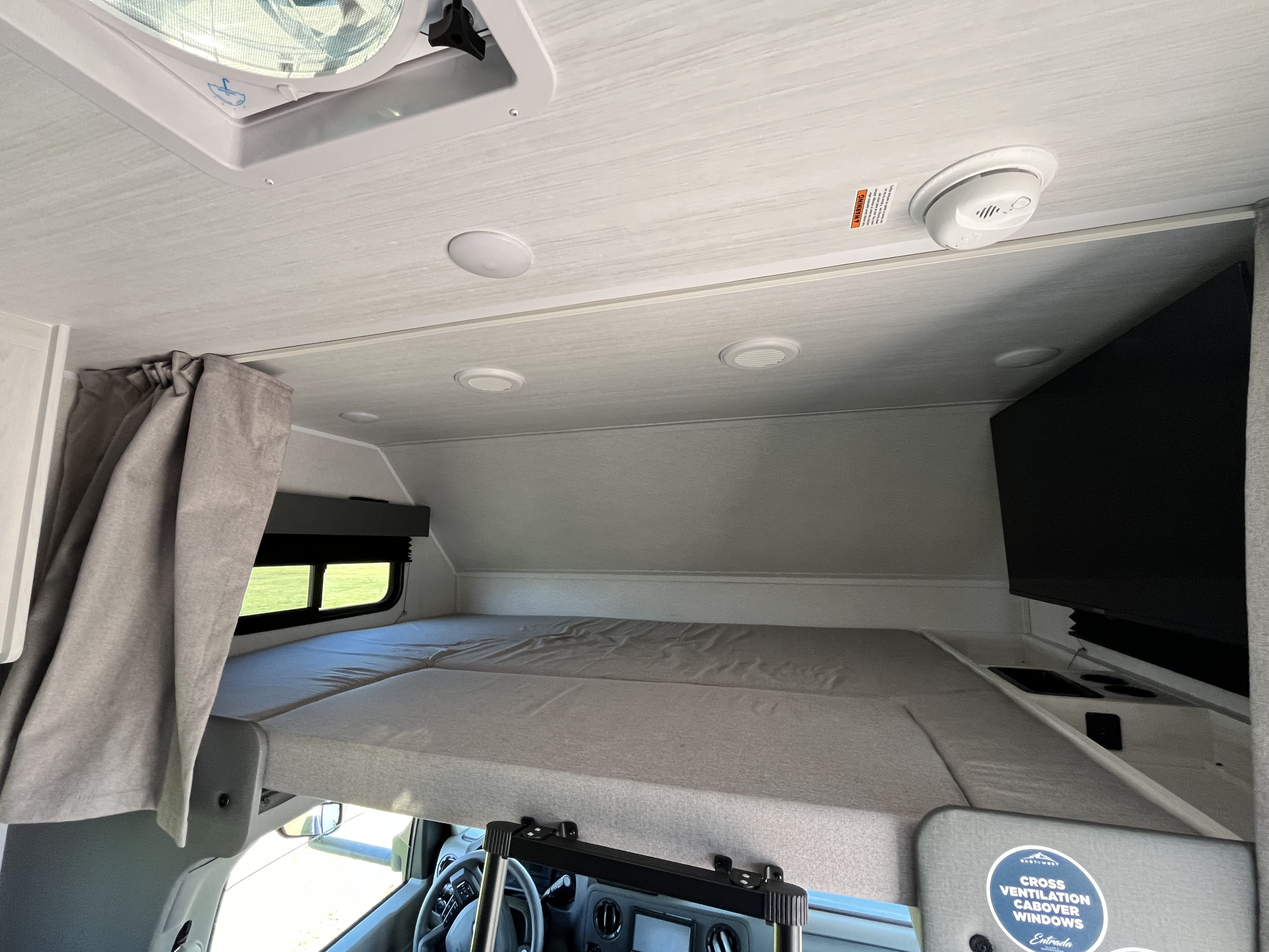 Experience comfort in this RV rental's cabover bunk. Features include a cozy bed, windows, ceiling fan, lights & smoke detector.. East to West Entrada 210NS 2025