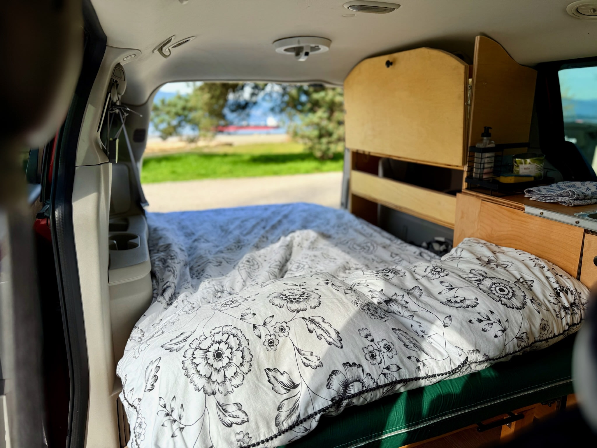 Cozy RV rental interior with a white floral bed and custom wooden storage. Scenic water view from the back.. Dodge Dodge Grand Caravan 2008