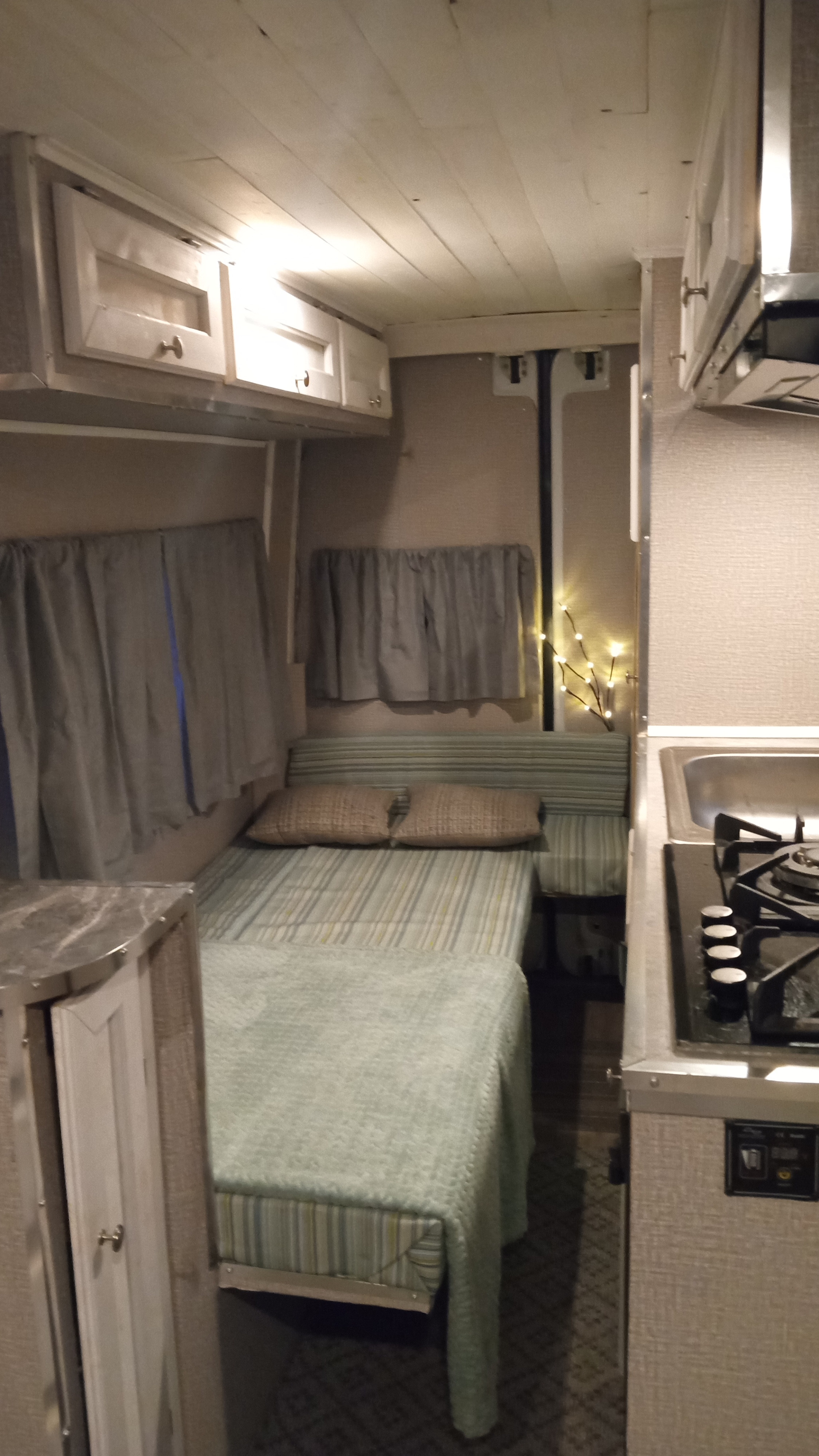 Cozy RV rental interior with a bed, kitchen (sink, stovetop), overhead cabinets, and soft lighting.. Mercedes Sprinter 3500 2010