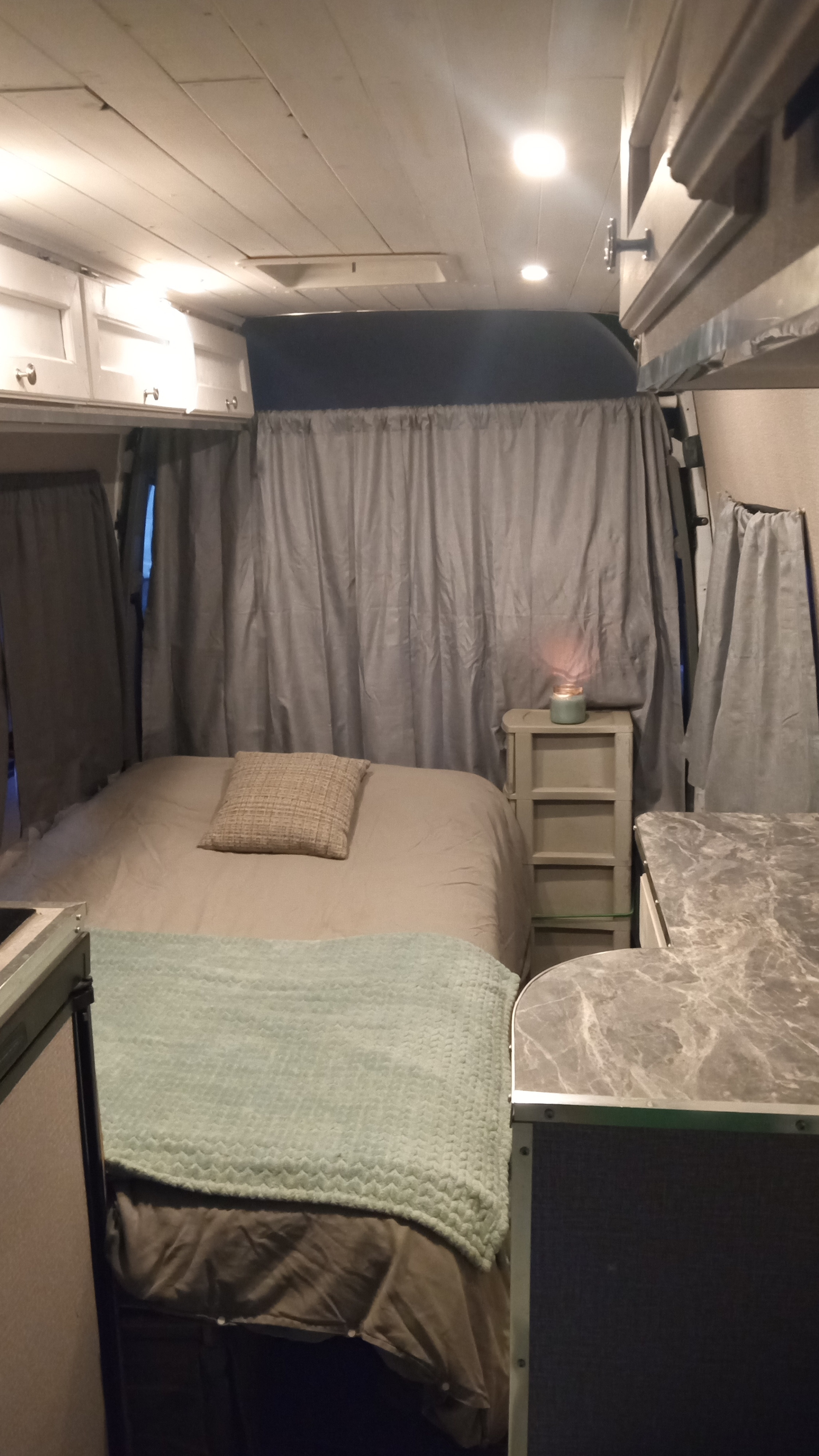 Explore a cozy RV rental's interior. Features a comfortable bed, warm lighting, and privacy curtains for travel.. Mercedes Sprinter 3500 2010