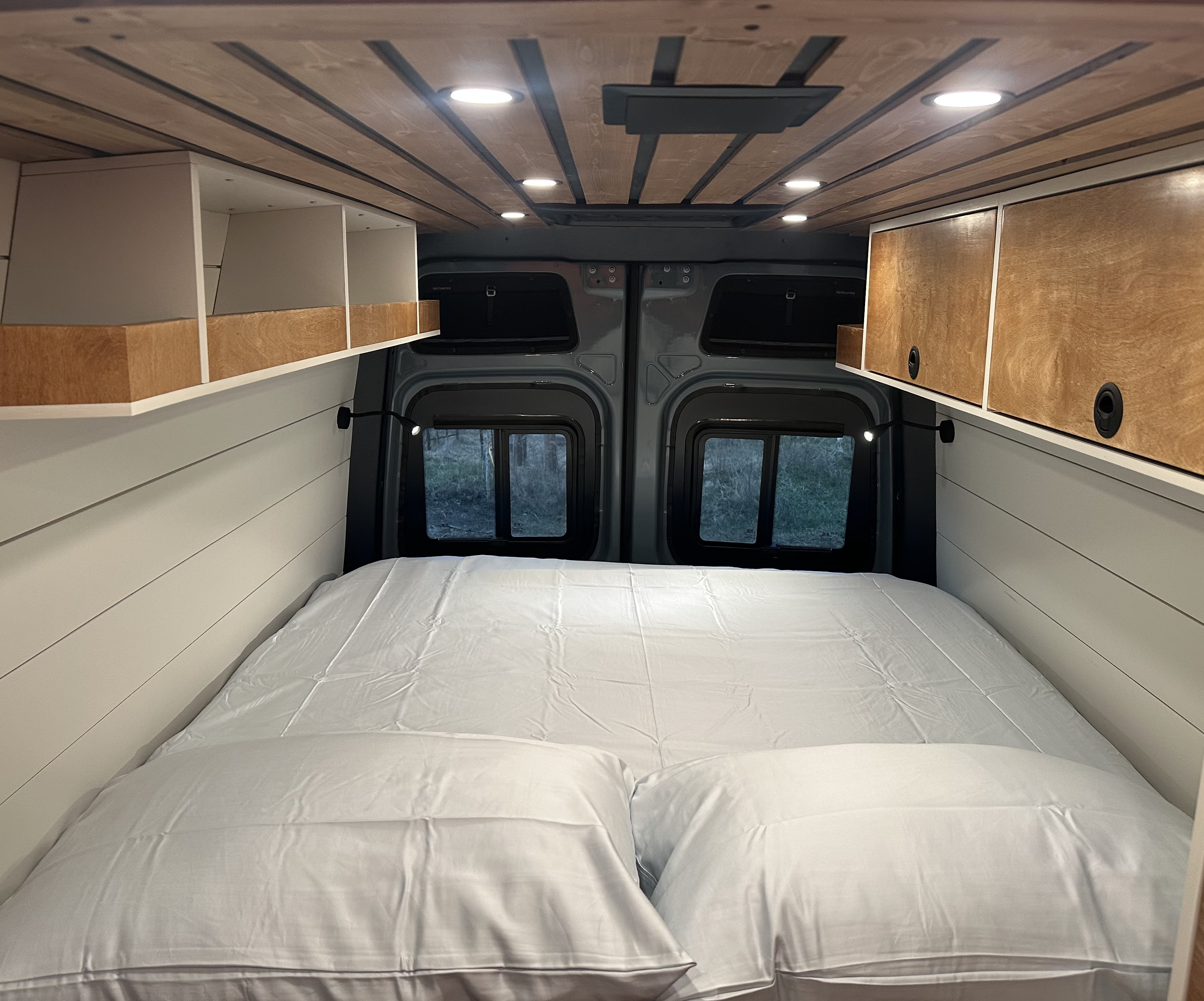 Cozy RV rental interior featuring a comfortable bed, built-in storage, stylish ceiling, and scenic rear windows.. Mercedes Sprinter 2024
