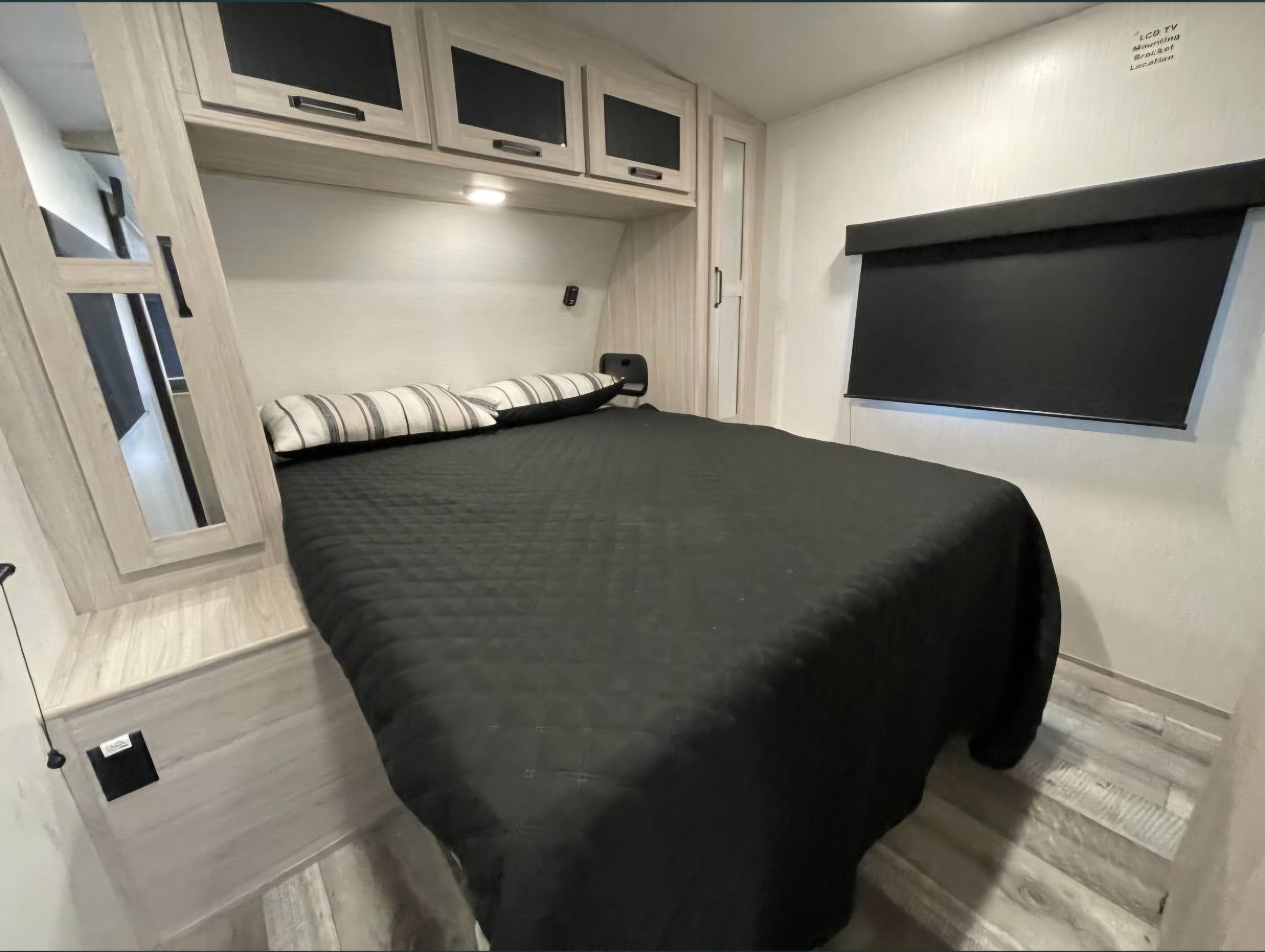 RV rental bedroom featuring a large bed, overhead storage, a mirrored wardrobe, and a prepped TV mounting area.. Heartland RVs Sundance Ultra Lite 2022