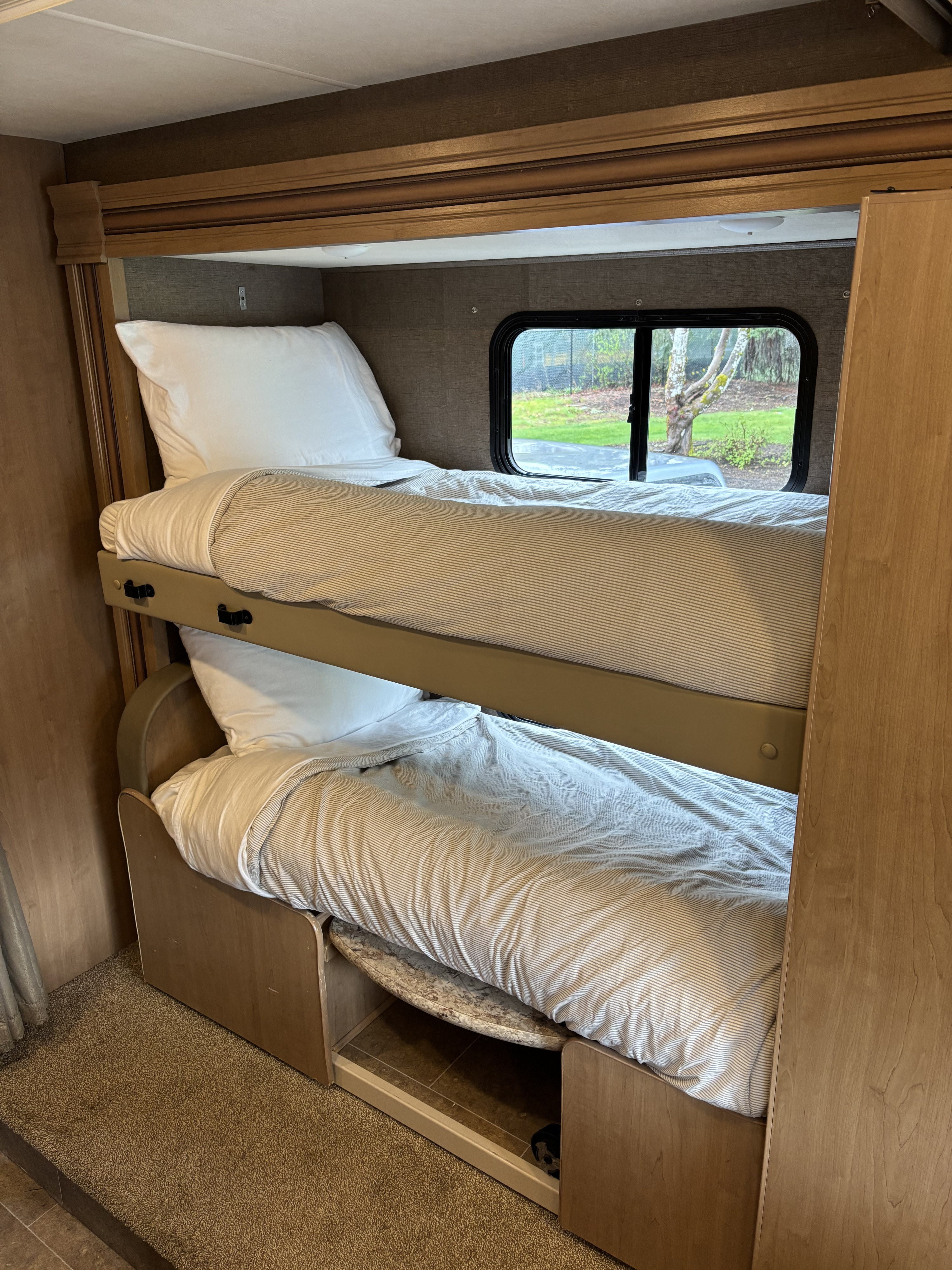Comfortable bunk beds in an RV rental, offering cozy sleeping space with striped bedding and a window view.. Thor Chateau 2019