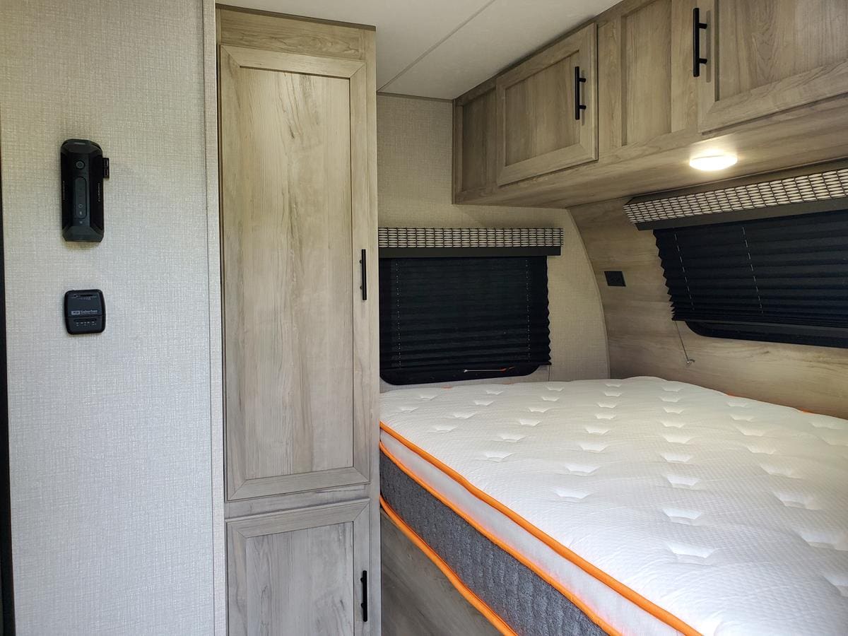 Inside an RV rental: a compact travel trailer bedroom featuring a cozy bed, overhead cabinets, and a wardrobe.. kz e17 2021