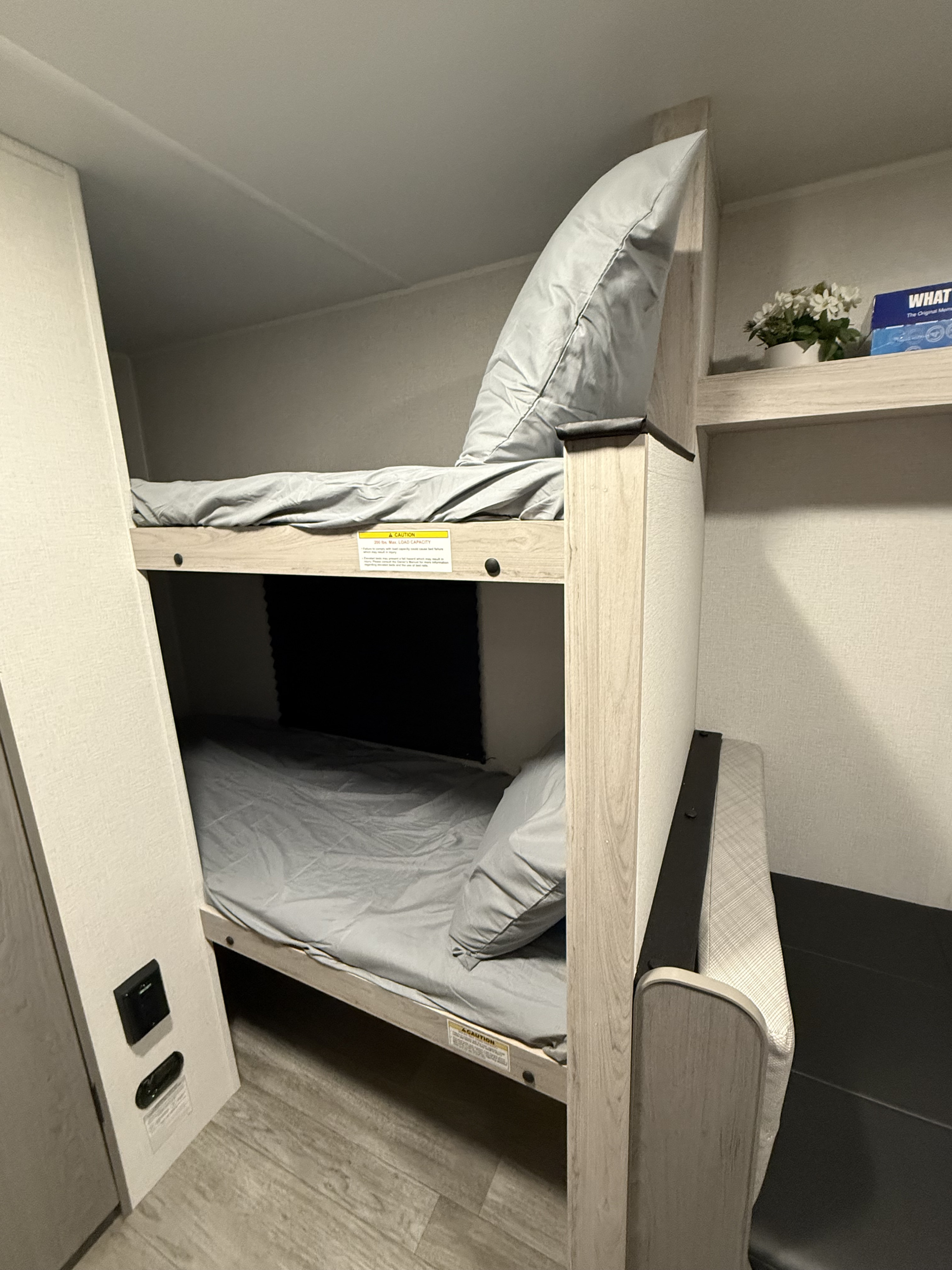 Cozy two-tier bunk beds with gray bedding and a built-in shelf in this RV rental.. Heartland Trail Runner 2025