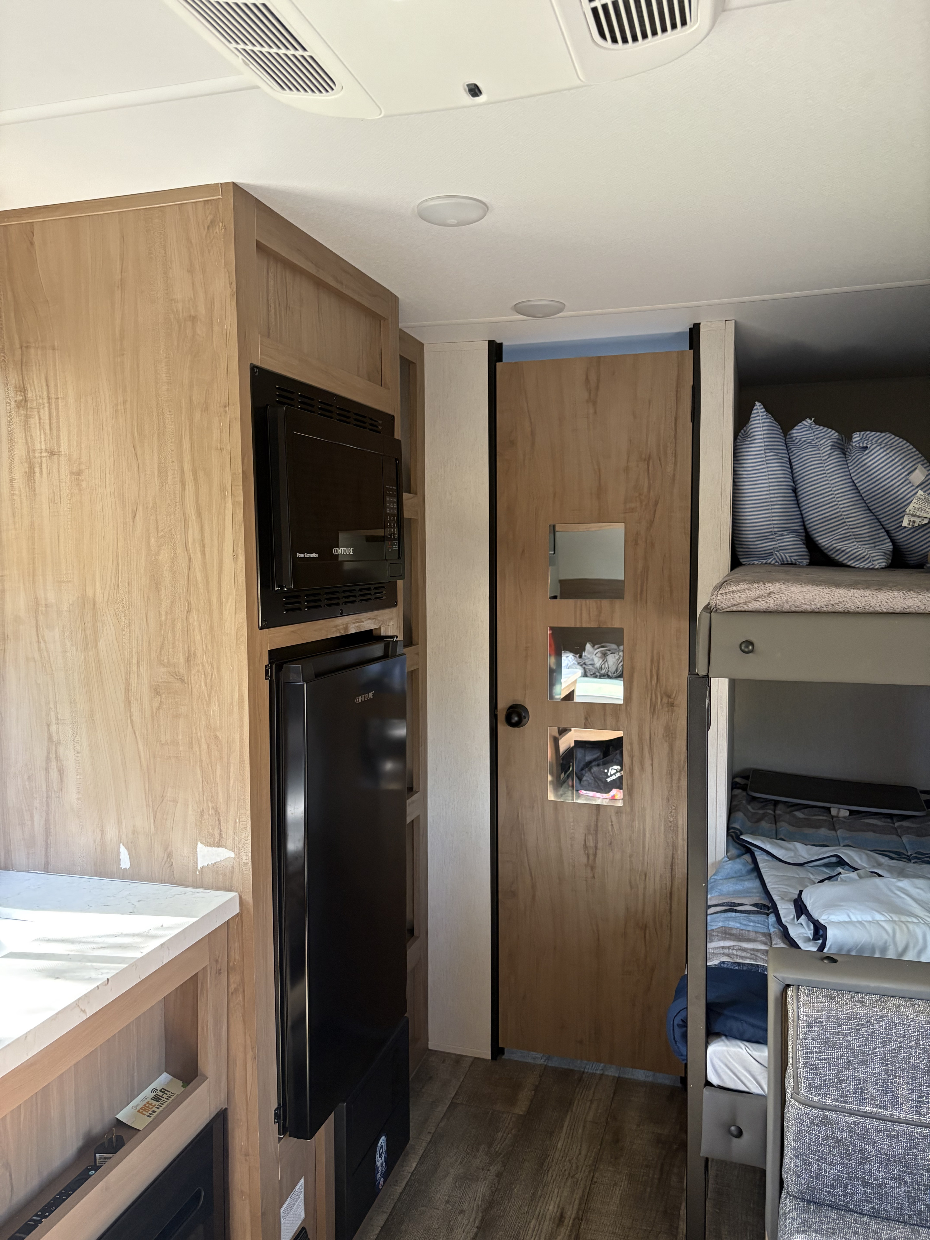 Experience comfort in this RV rental interior: featuring a light wood kitchen with microwave, fridge, and bunk bed area.. Forest River Cherokee Wolf Den 16EV 2024