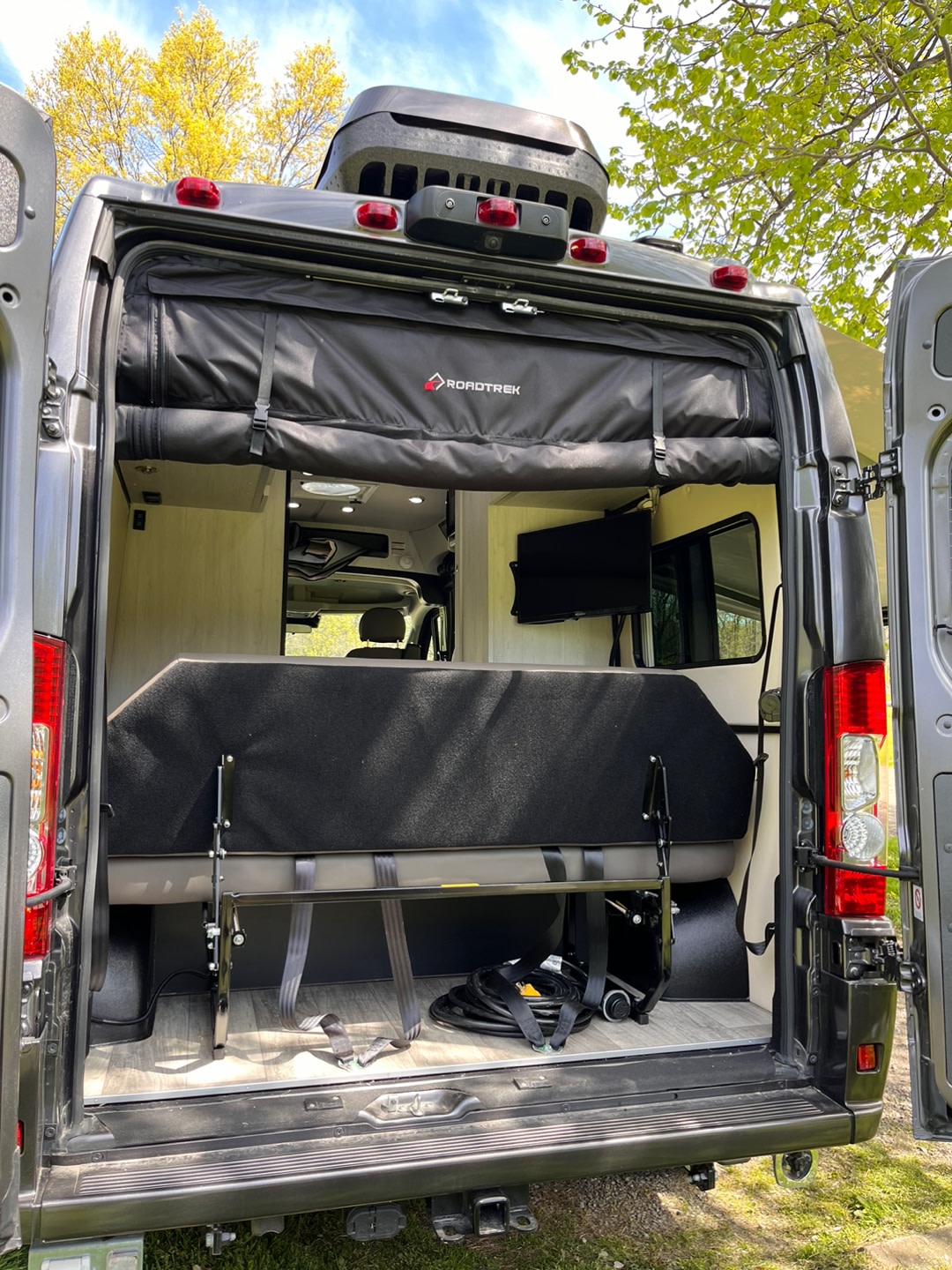 This RV rental campervan reveals its versatile rear interior, featuring a bed/bench, TV, and overhead Roadtrek storage.. Roadtrek Roadtrek Class B 2024