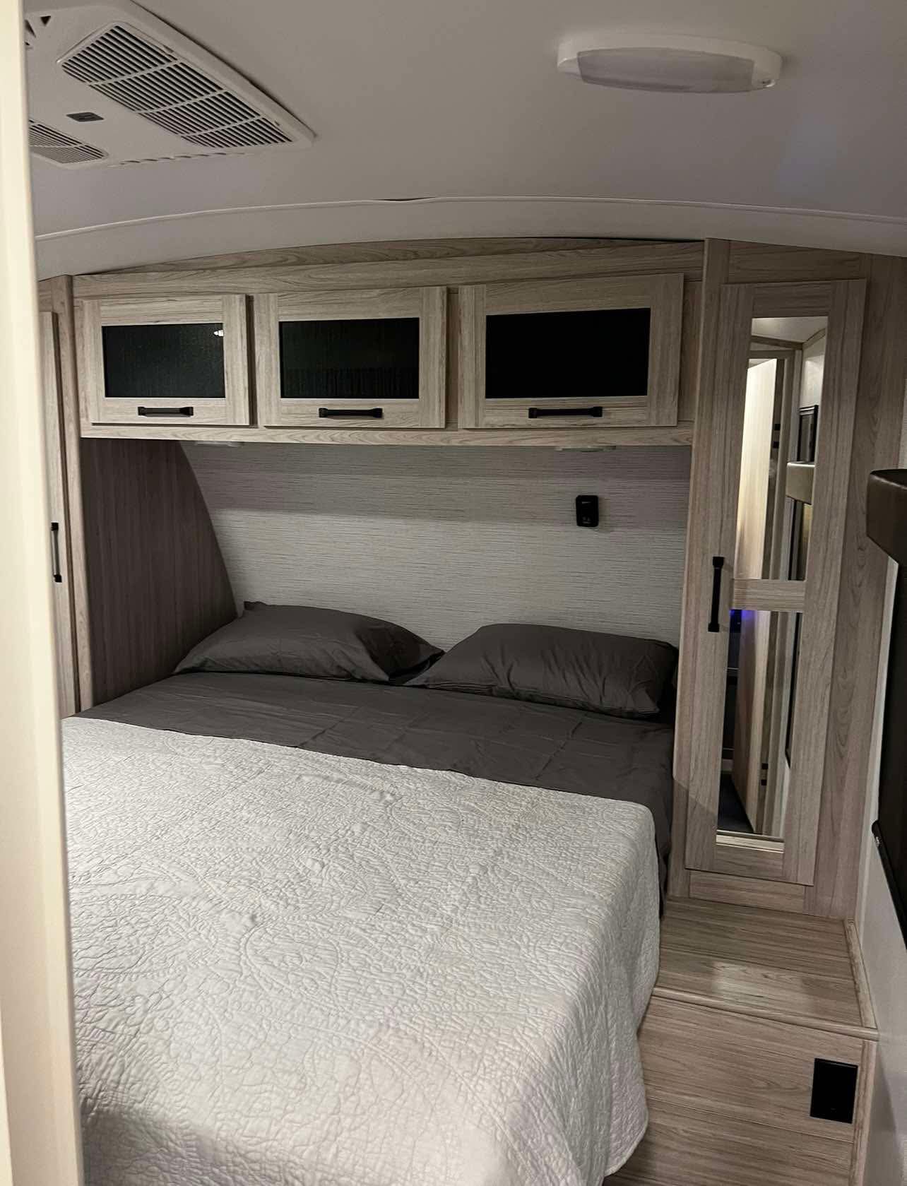 RV rental bedroom with light wood cabinetry, overhead AC unit, and a neatly made bed for a comfortable stay.. Heartland Sundance 2022
