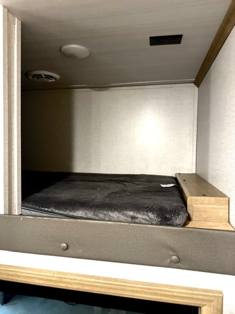 Inside an RV rental: a cozy bunk bed with a soft mattress. Notice the ceiling light and air vent for comfort in this compact sleeping space.. keystone 423 2022