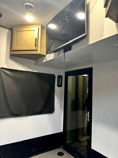 RV rental interior: A wooden cabinet, wall-mounted TV, and a glass-paneled door in a modern RV living space.. keystone 423 2022