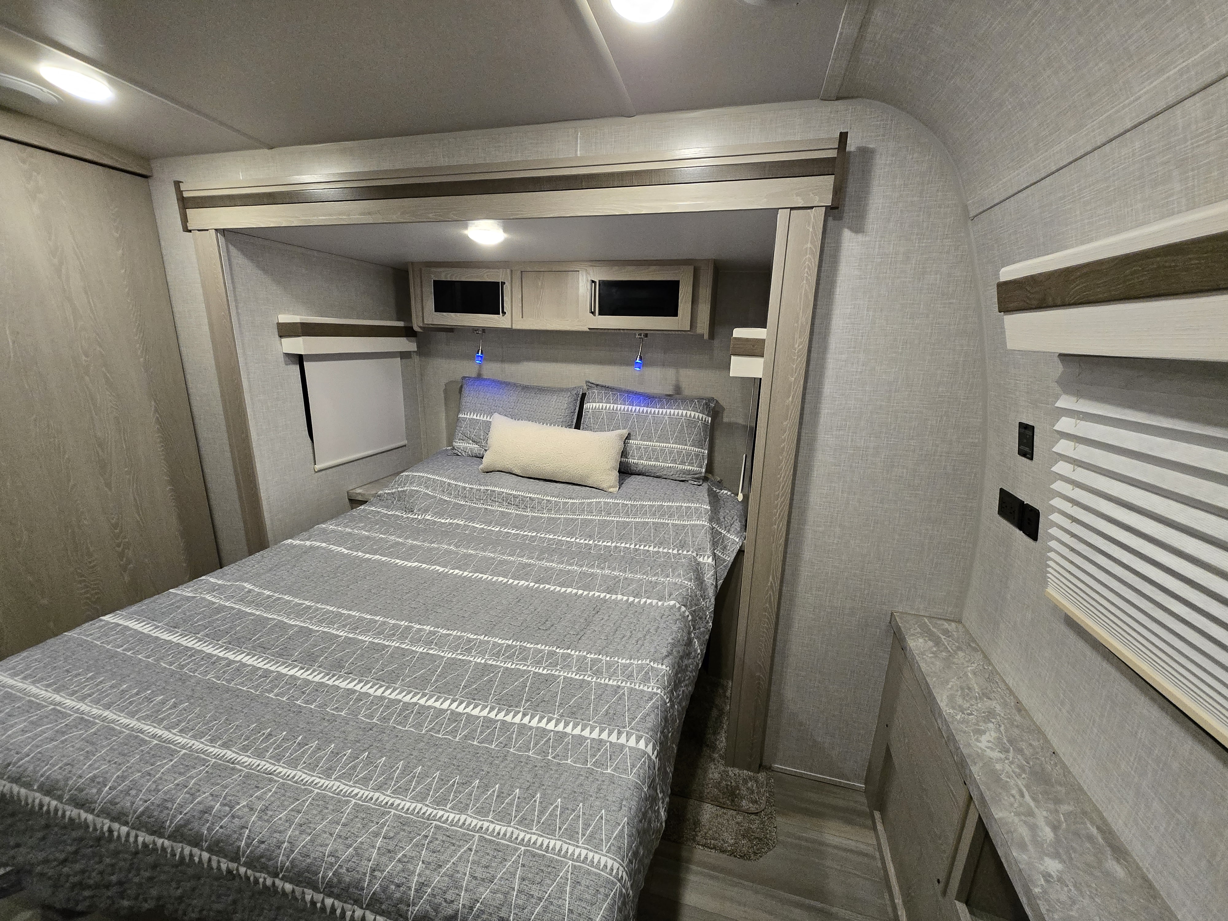 Cozy modern RV rental bedroom with gray patterned bedding, overhead storage, and accent lights.. Forest River Rockwood Ultra Lite 2022
