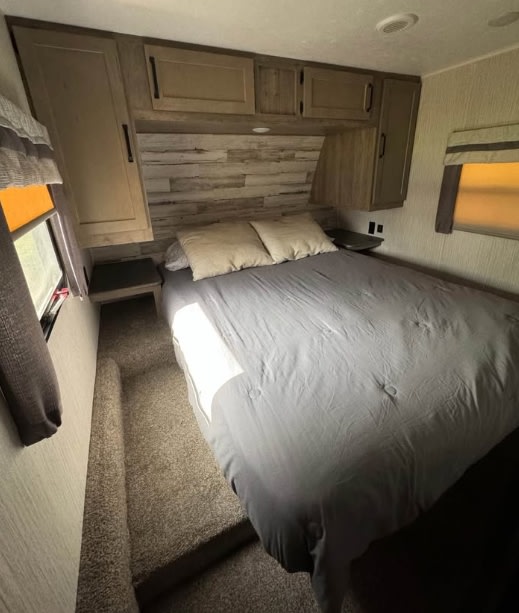 RV rental bedroom with a large bed, gray comforter, wood-look headboard, and overhead storage cabinets.. Palomino Puma 2022