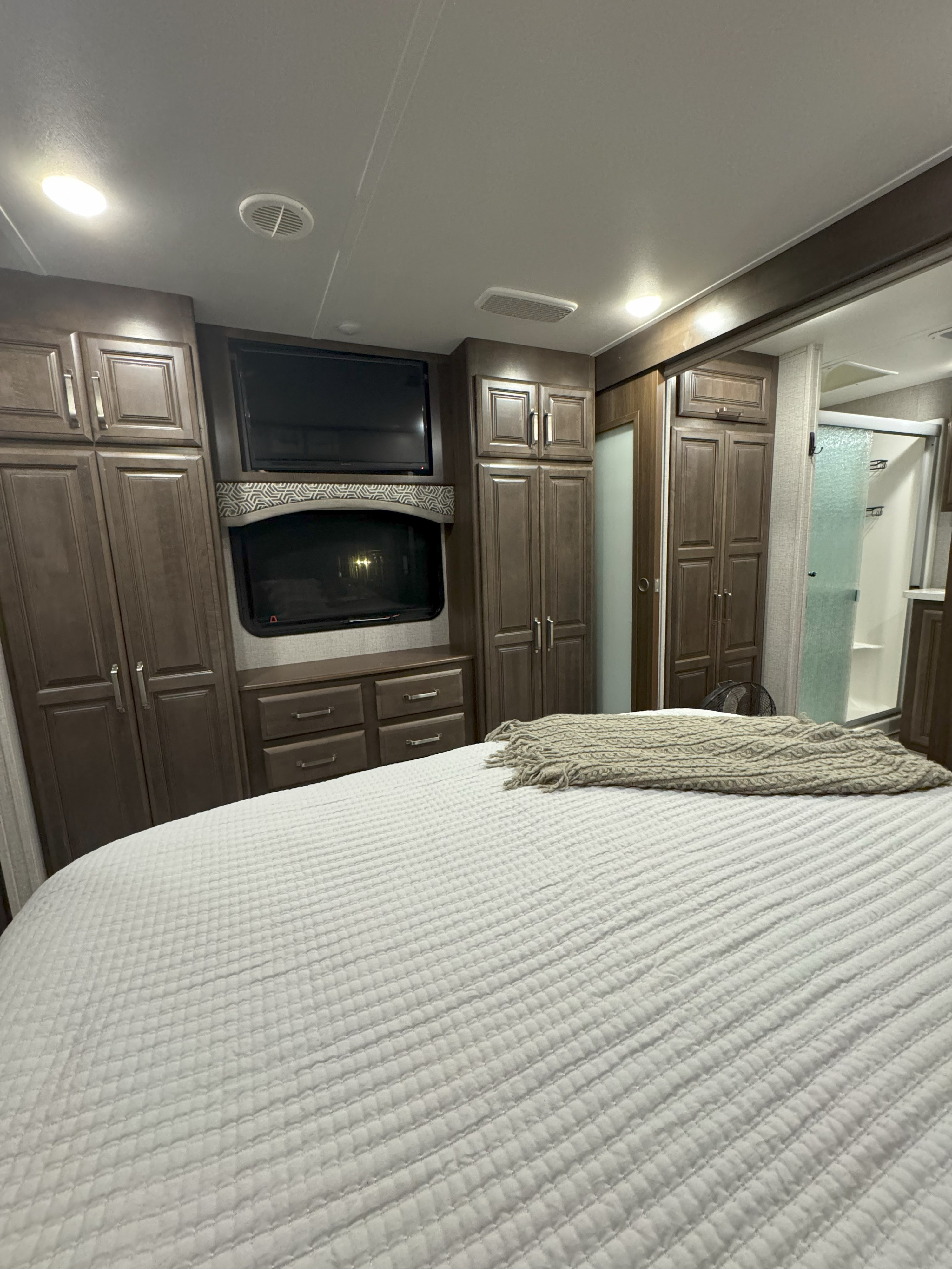 Spacious RV rental bedroom with comfortable bed, ample storage cabinets, dual TVs, and an ensuite shower visible.. Keystone RV Alpine 2020