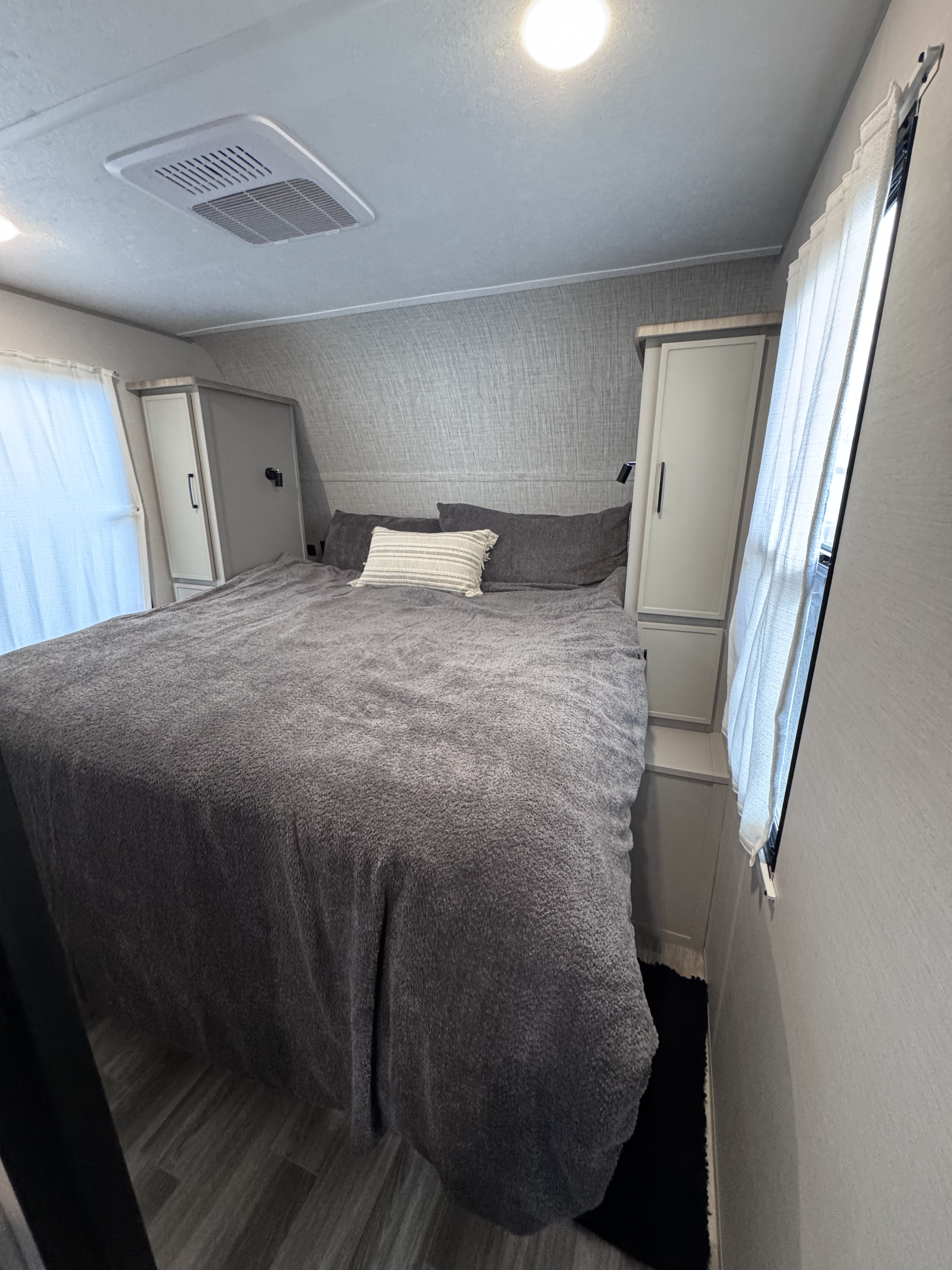 Spacious RV rental bedroom featuring a comfy grey bed, dual side wardrobes, windows with curtains, and an overhead AC unit.. Forest River Vibe 2025