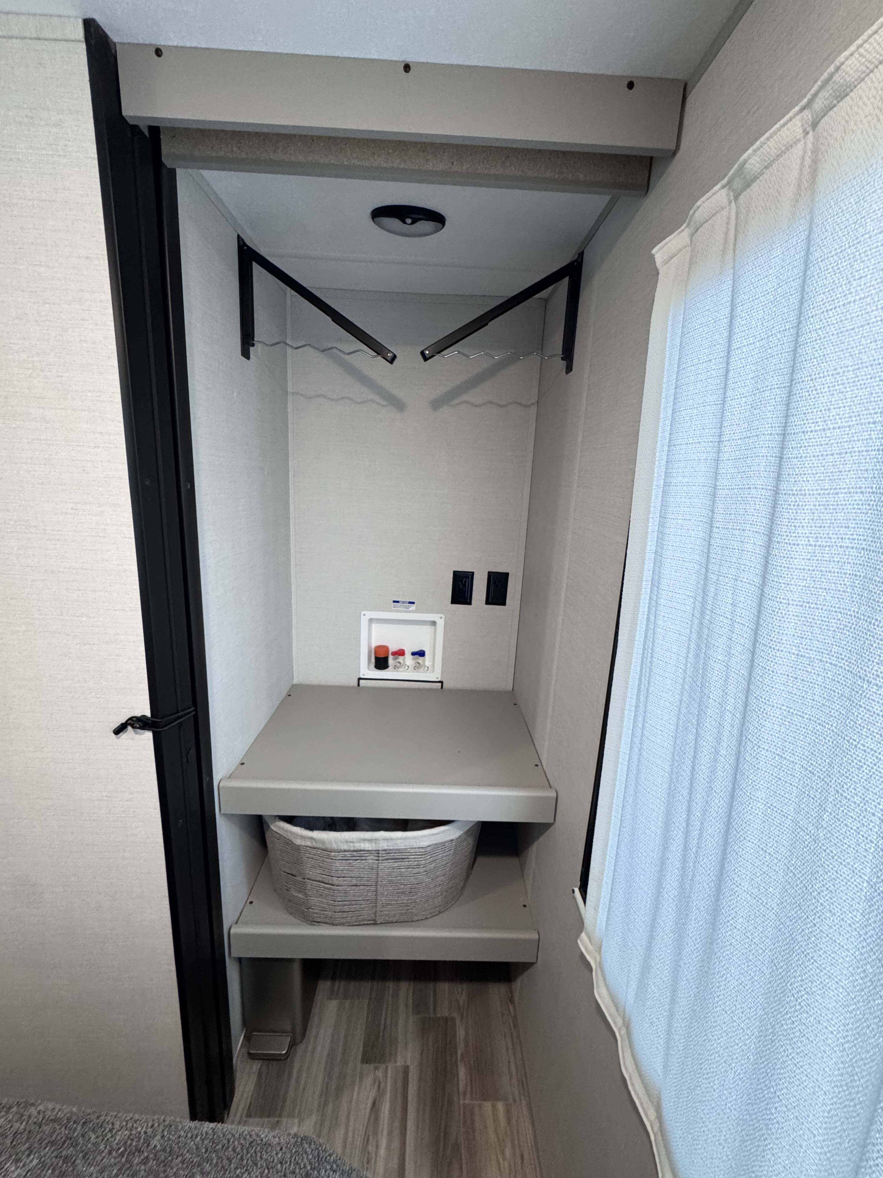 Inside an RV rental: a compact laundry nook featuring washer/dryer hookups, shelves, and clothes hanging rods.. Forest River Vibe 2025
