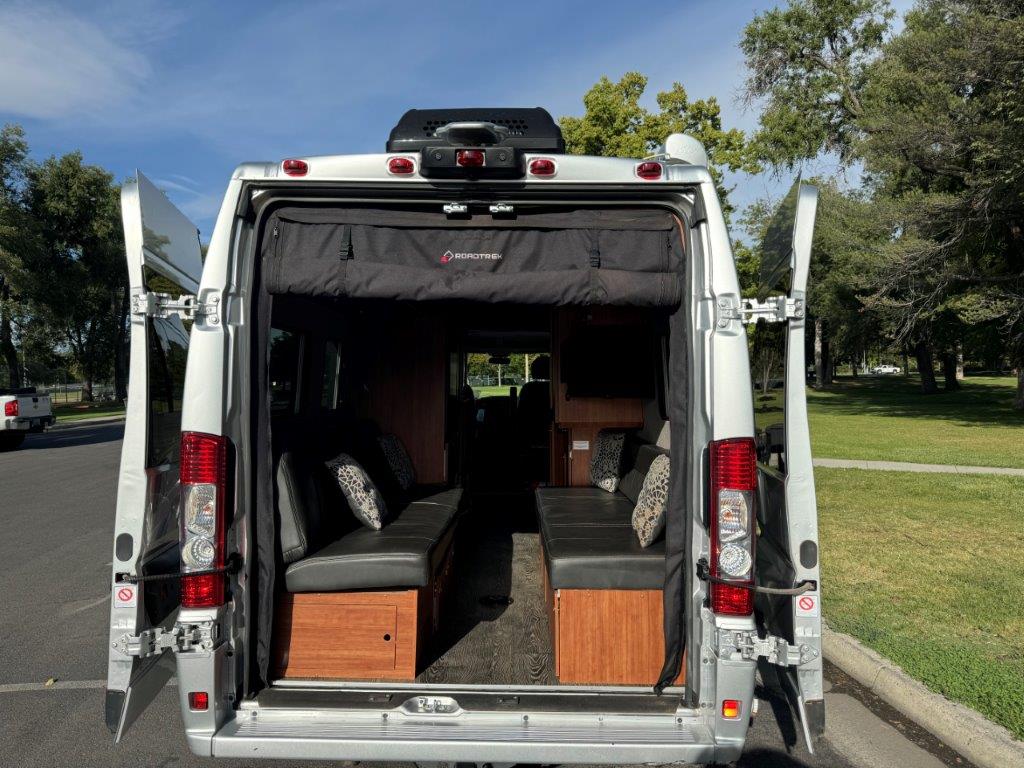 Inside an RV rental van: rear doors open to a comfy camper interior with facing black benches and pillows.. Roadtrek Roadtrek Class B 2021