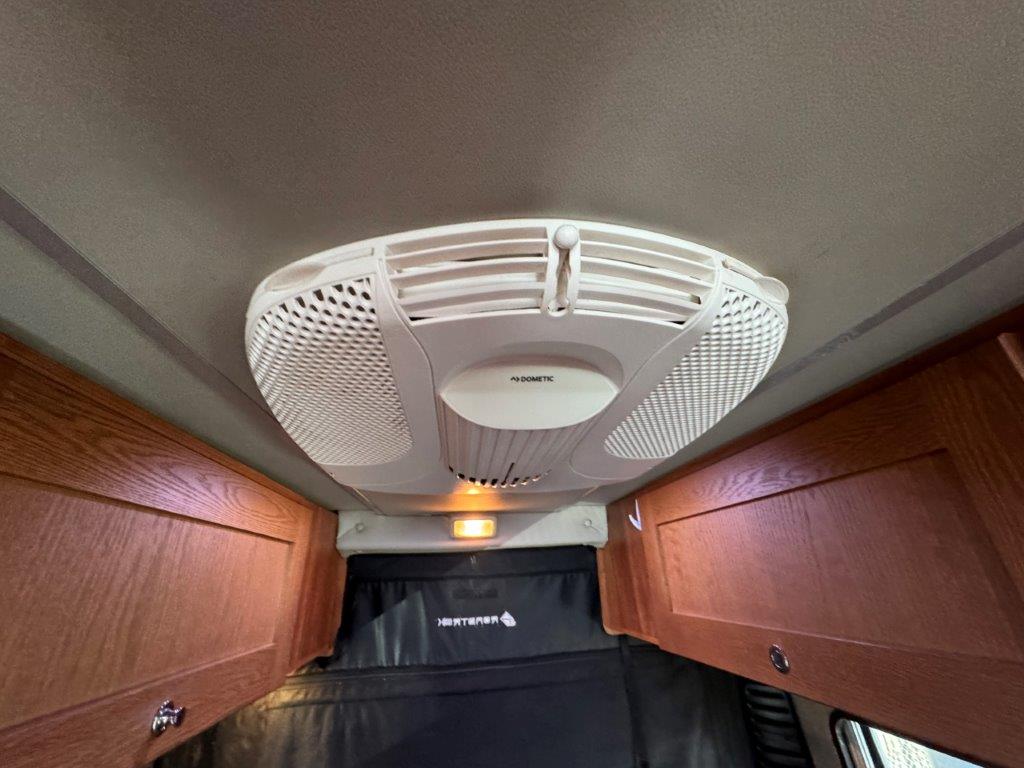 Inside an RV rental: a Dometic air conditioner on the ceiling, surrounded by wood cabinets, ensuring comfort.. Roadtrek Roadtrek Class B 2021