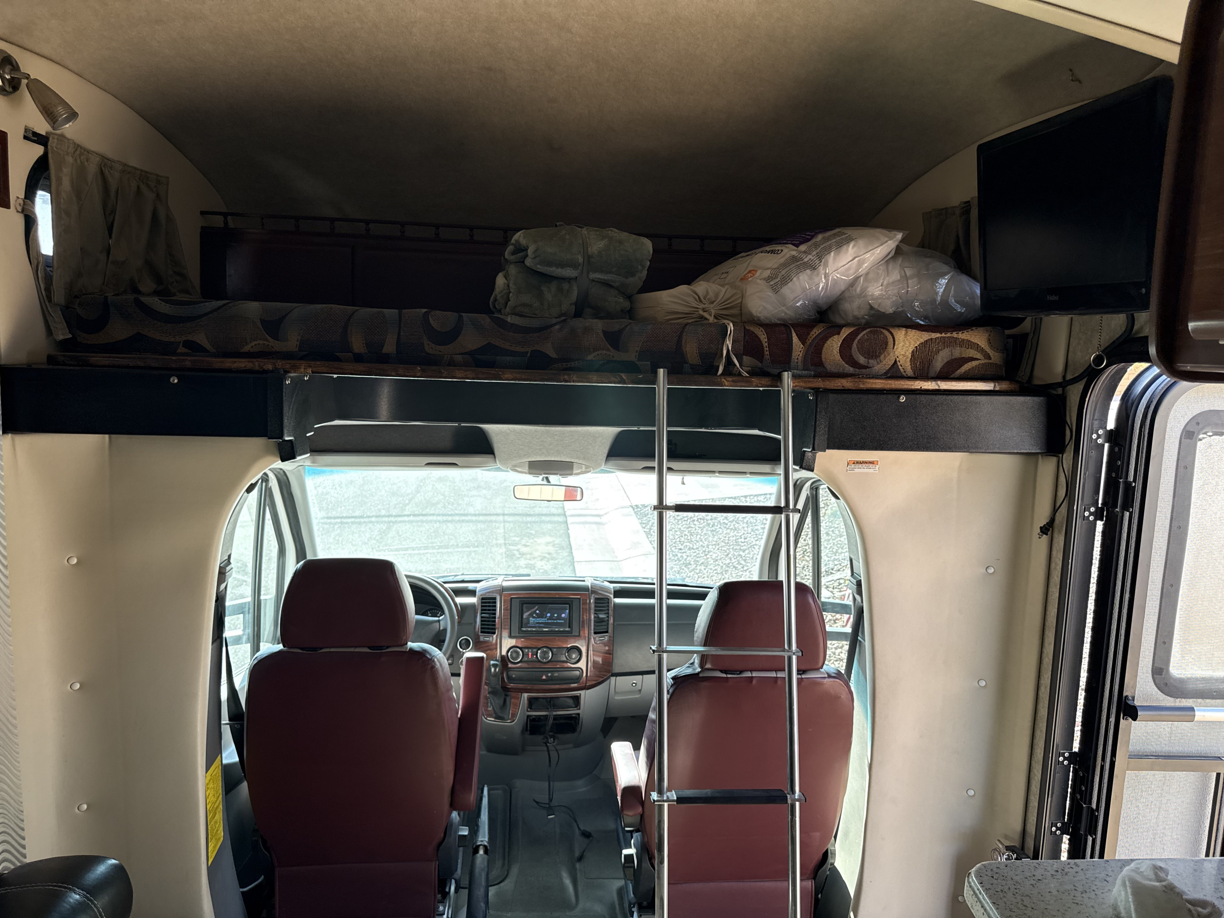 This RV rental interior features a cab with two seats, a dashboard, and an overhead bunk bed accessible by ladder.. Fleetwood Tioga 2011