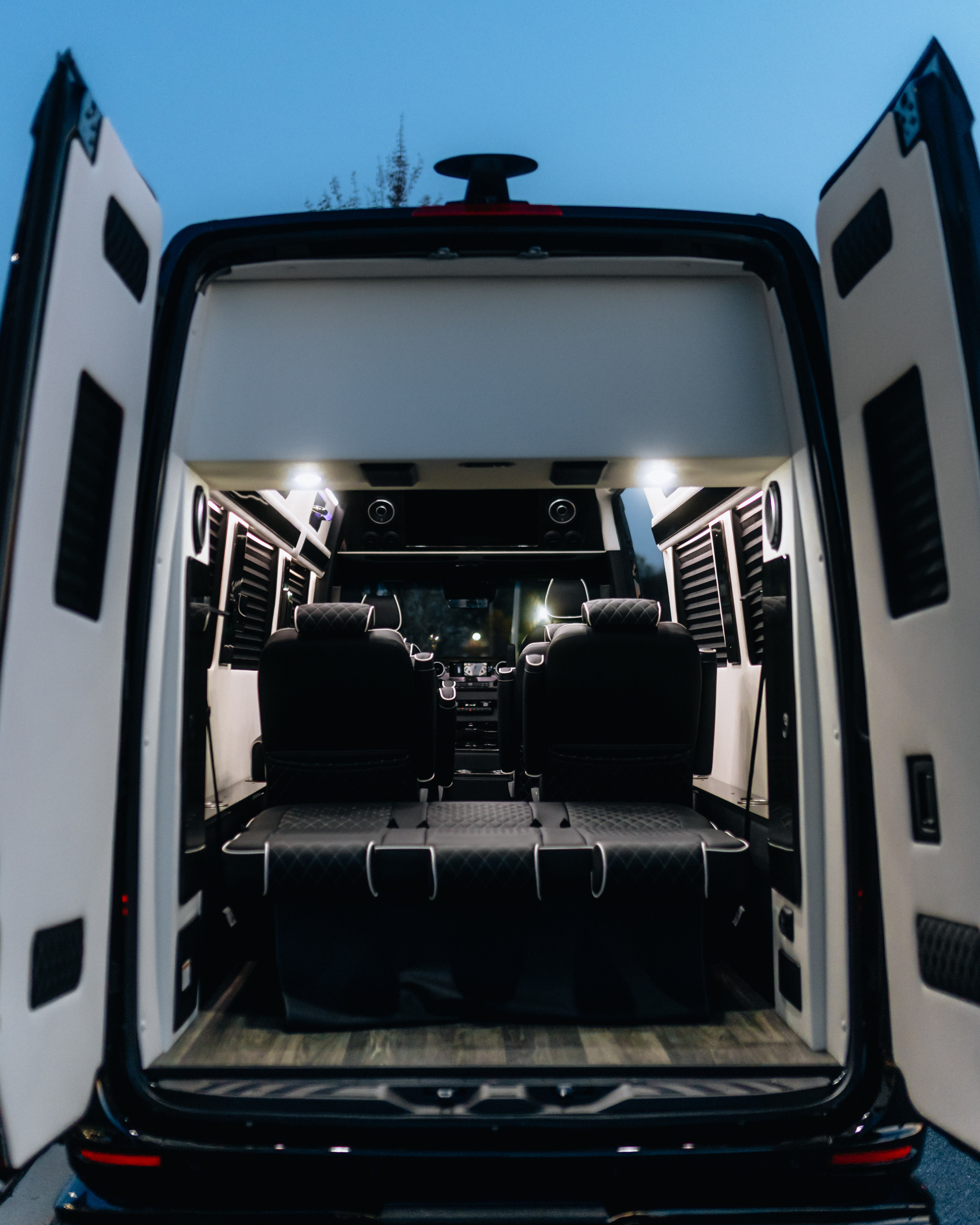 Rear view of a premium RV rental interior featuring black leather seating, a convertible bed, and elegant wood flooring under bright lights.. Ultimate Toys Ultimate Freedom XL 2025