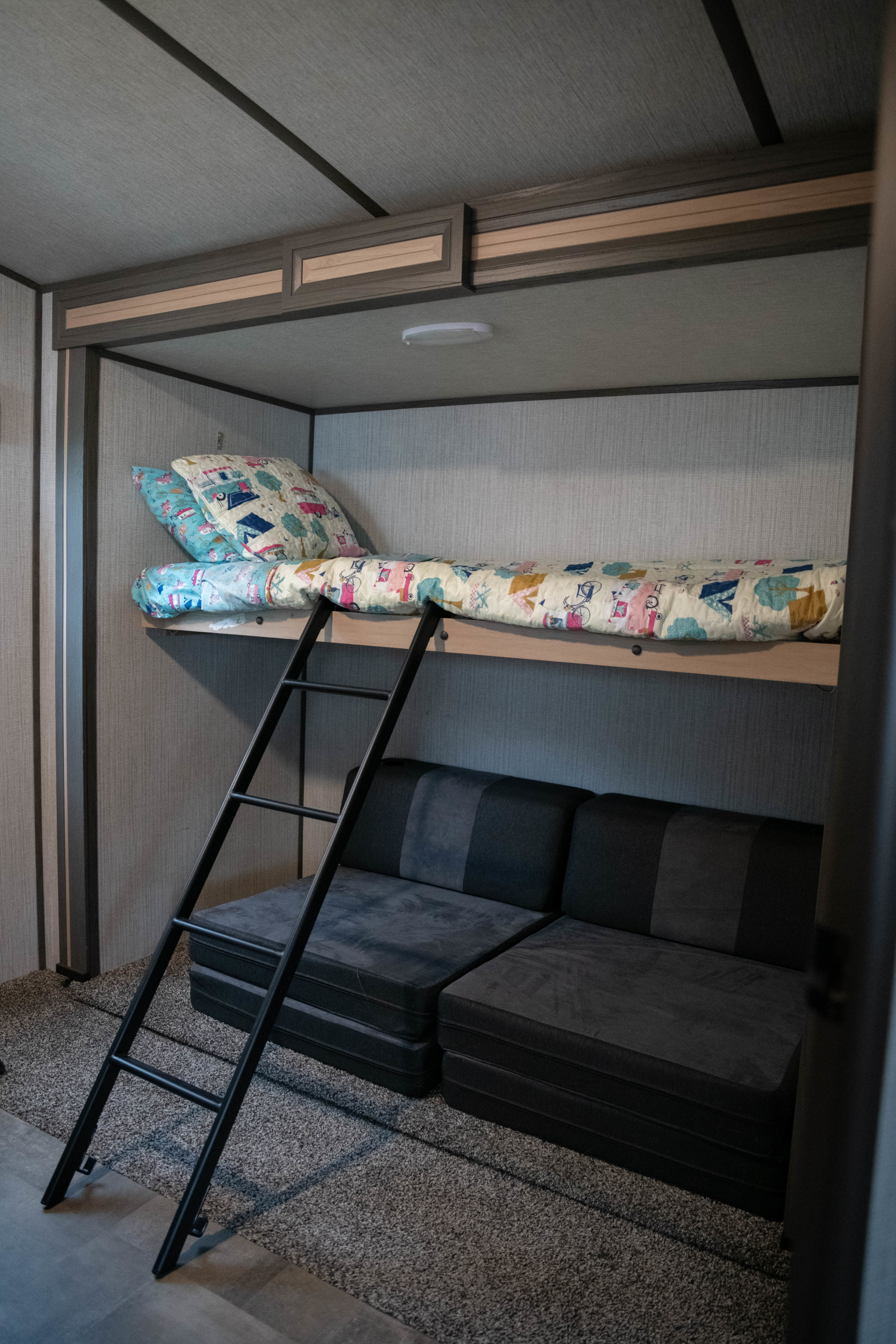 RV rental bunk bed with colorful bedding, a ladder, and dark grey modular seating below for compact sleeping.. Cruiser RV Radiance Ultra Lite 2020