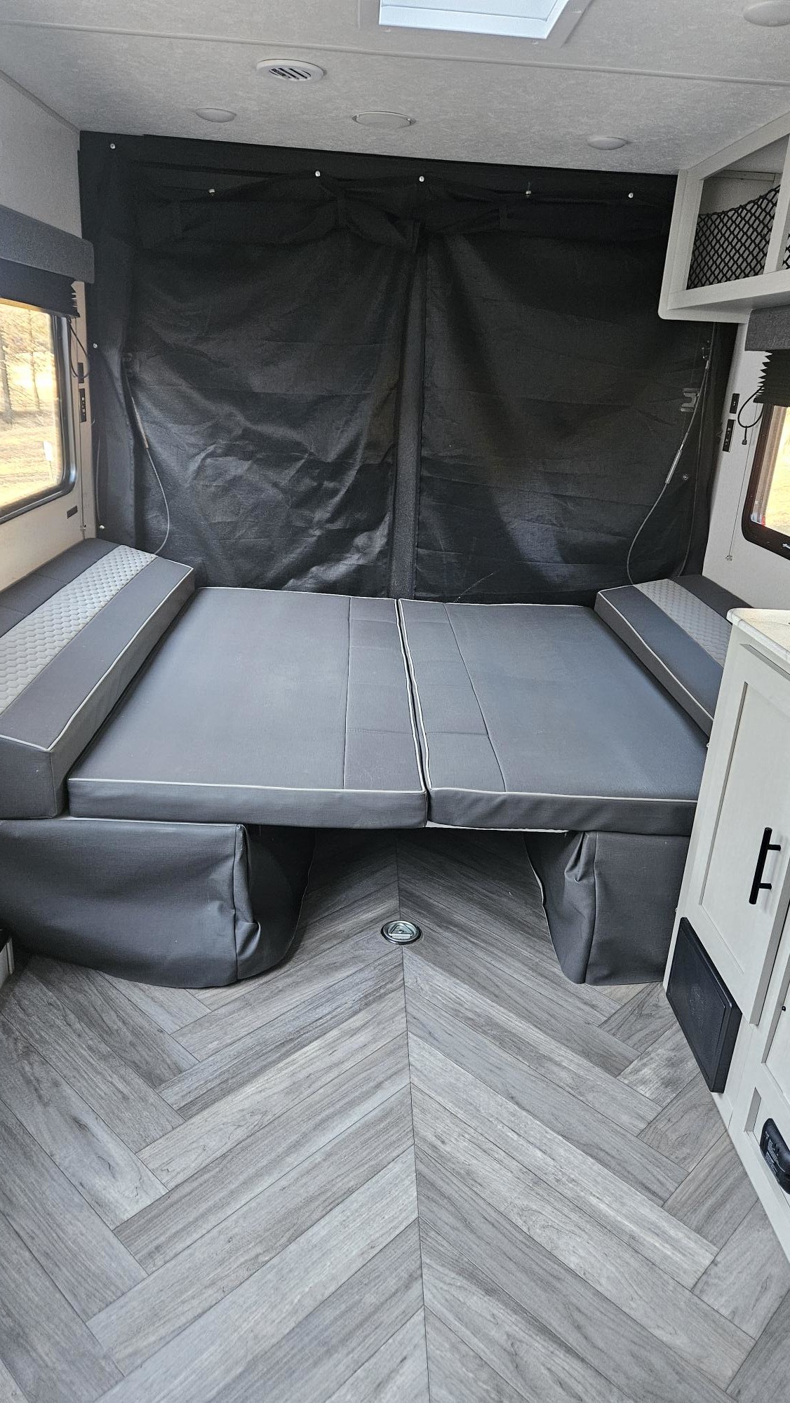 Cozy RV rental interior: A grey modular bed with side cushions, herringbone flooring, and black fabric rear wall.. Forest River Salem 2022