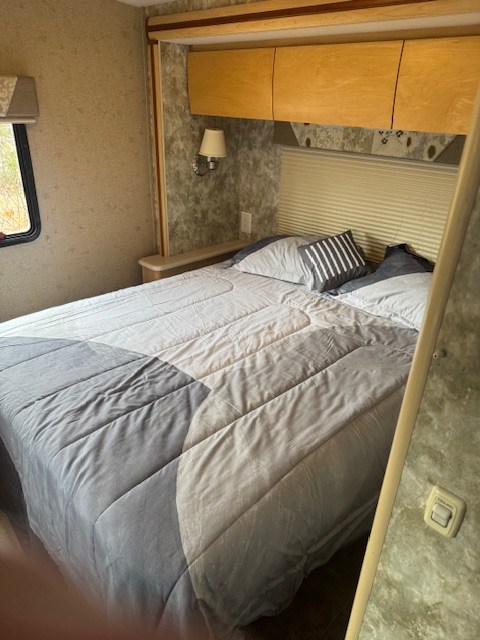 This RV rental features a comfortable bedroom with a patterned comforter, overhead storage, and a reading light.. Winnebago Outlook 2008