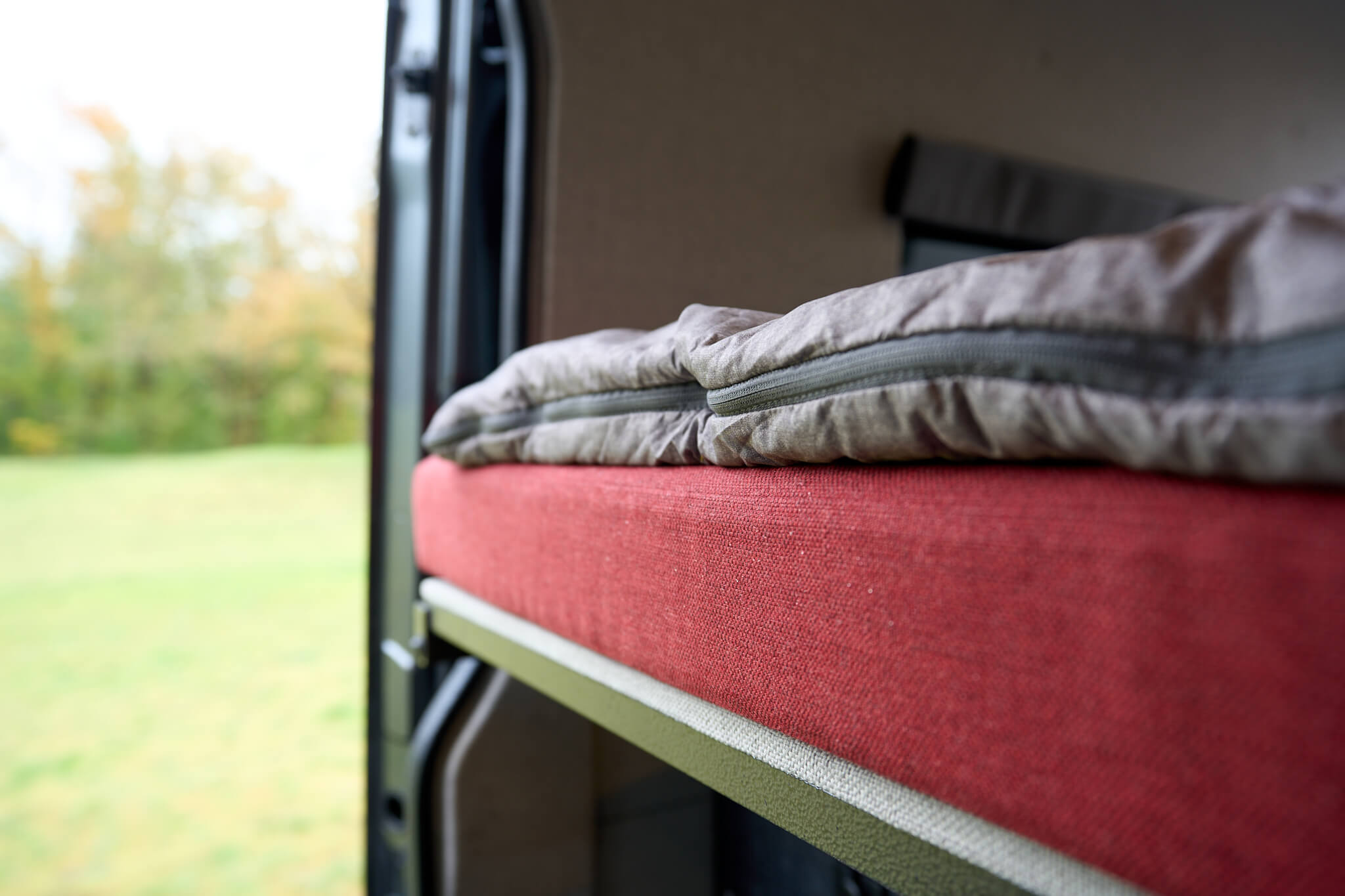 RV rental interior: A red-cushioned bed with folded sleeping bag, revealing green nature outside for adventure.. Mercedes-Benz Sprinter 2022