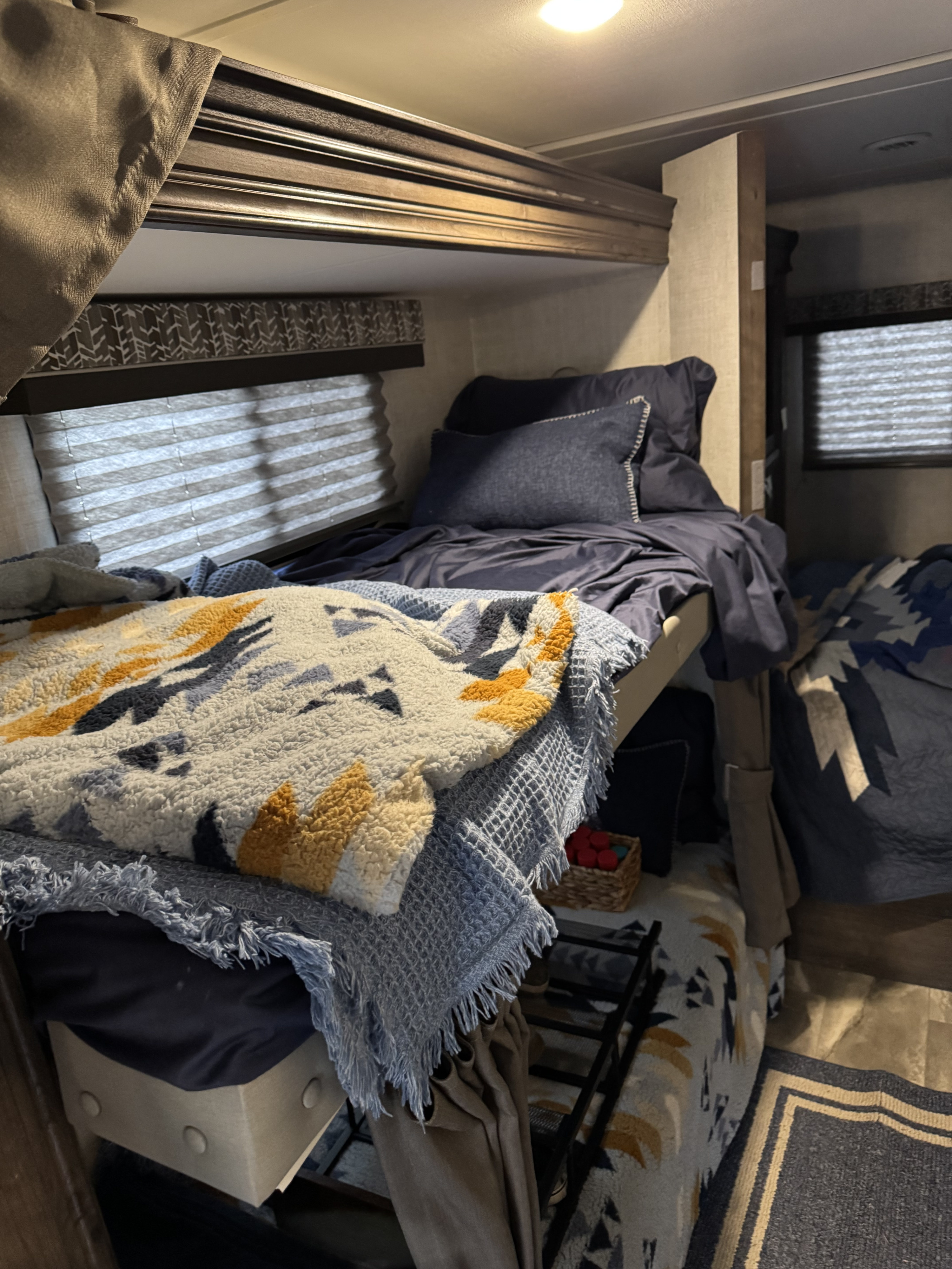 An RV rental bedroom featuring two bunk beds with blue and patterned blankets, and blinds on the windows.. Gulf Stream Conquest 2022