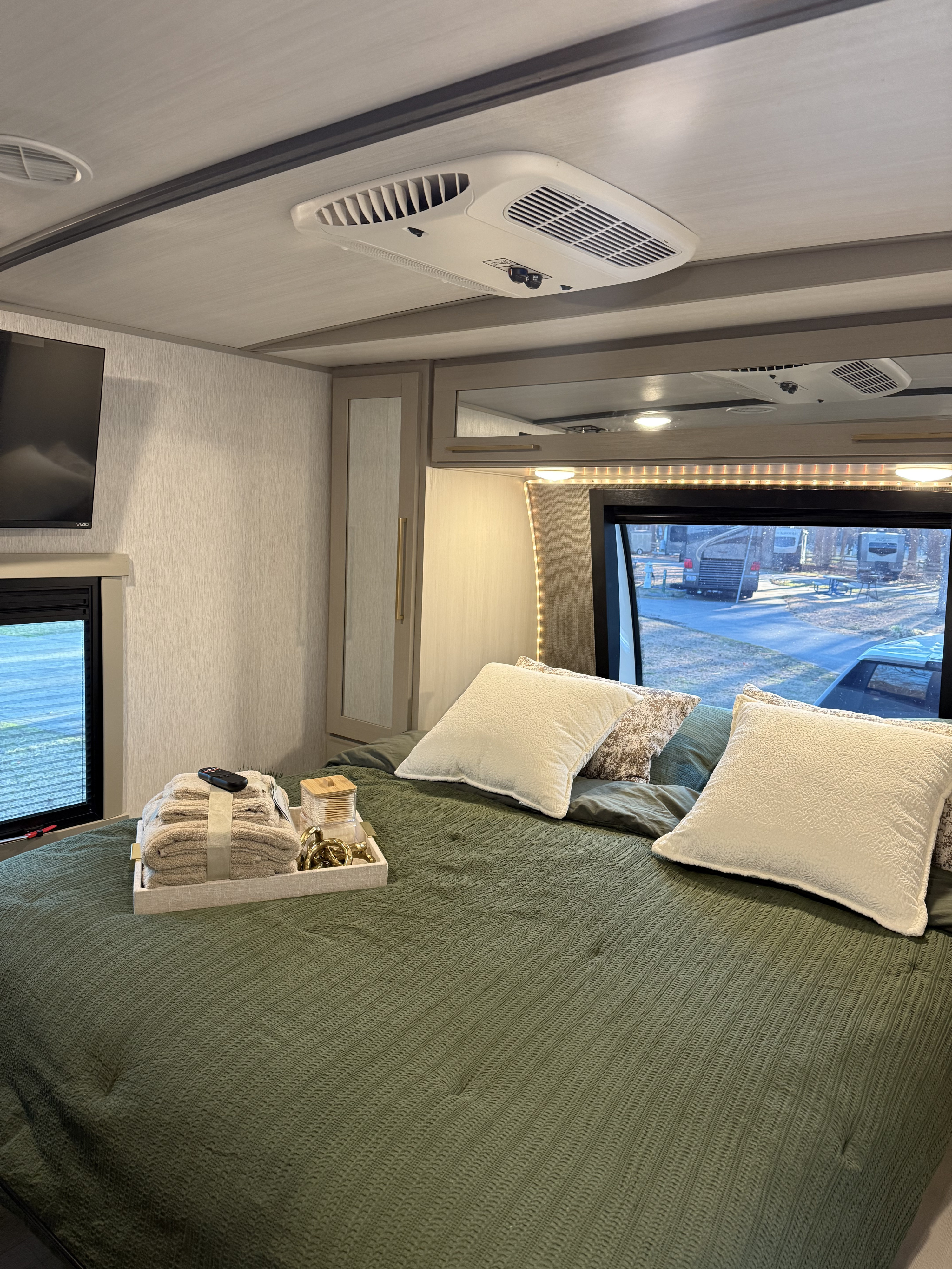 Cozy RV rental bedroom: a green bed with white pillows, ceiling AC, TV, and a window overlooking a campground setting.. Forest River Salem Hemisphere 2024