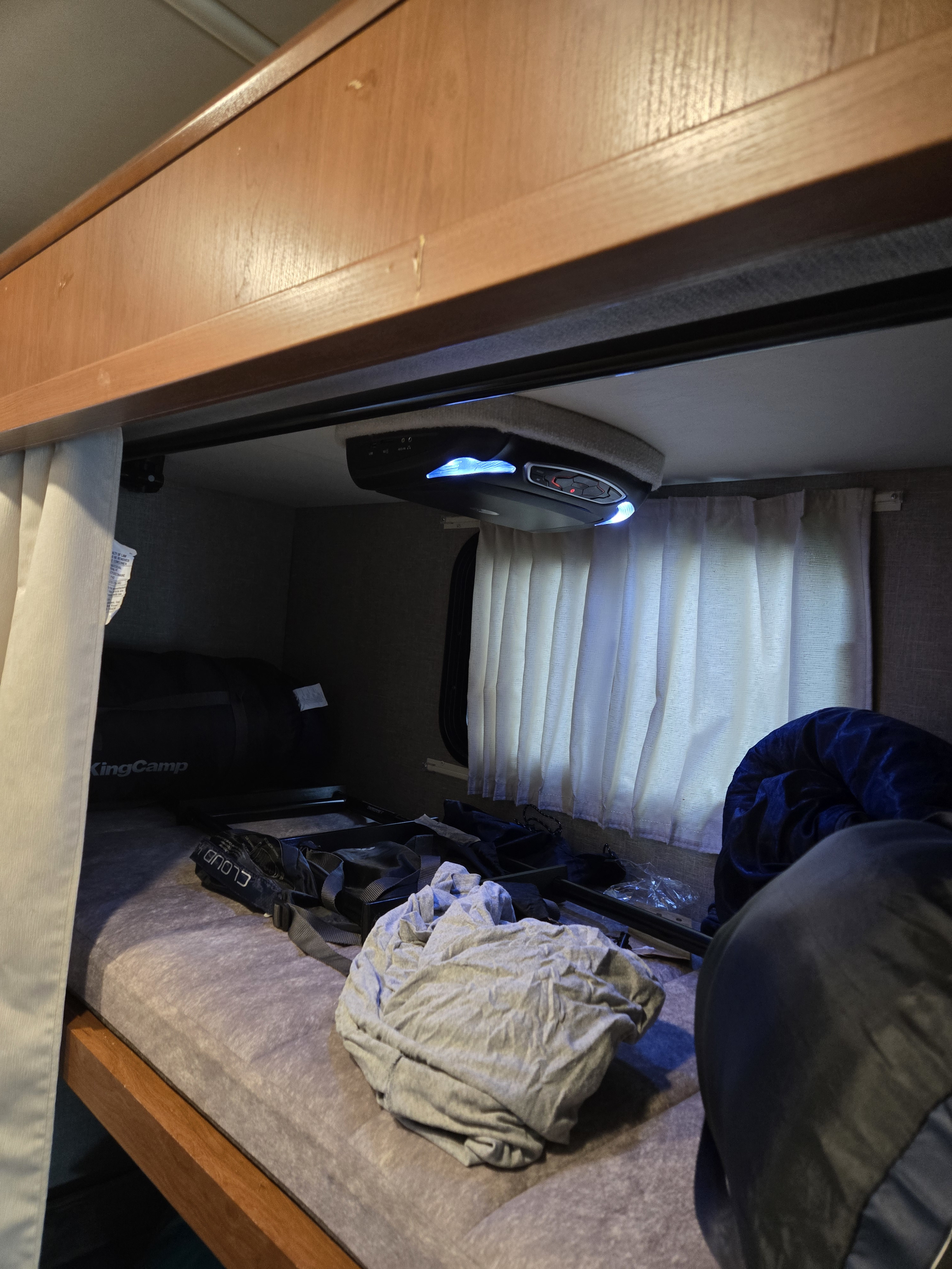 View of an RV rental bunk bed: cozy mattress, curtains, and an overhead entertainment system with blue lights.. Winnebago Sunstar 2019
