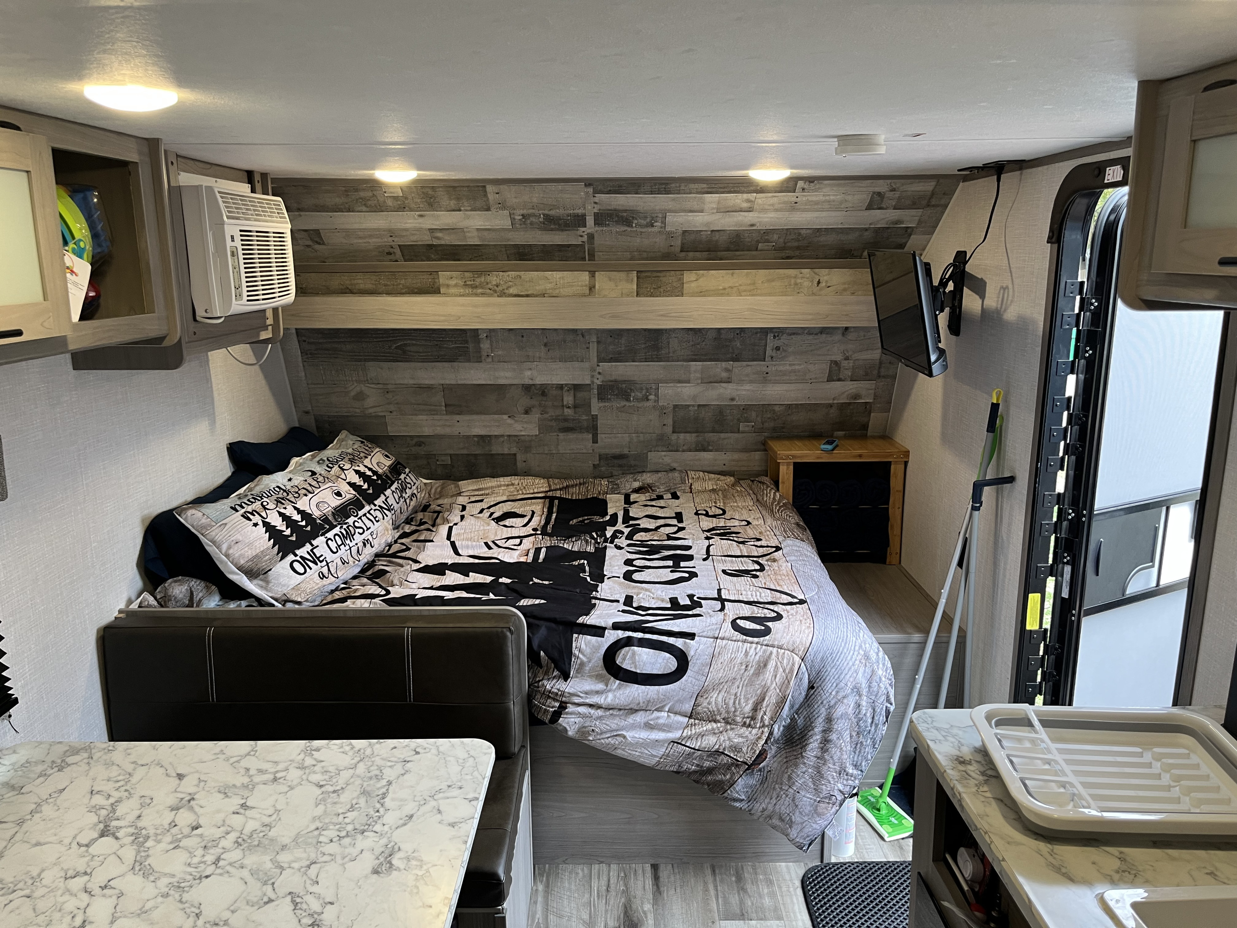 Cozy RV rental interior: bedroom area with a themed comforter, dinette, mounted AC unit, TV, and compact kitchen.. Dutchmen Coleman Lantern LT 2023
