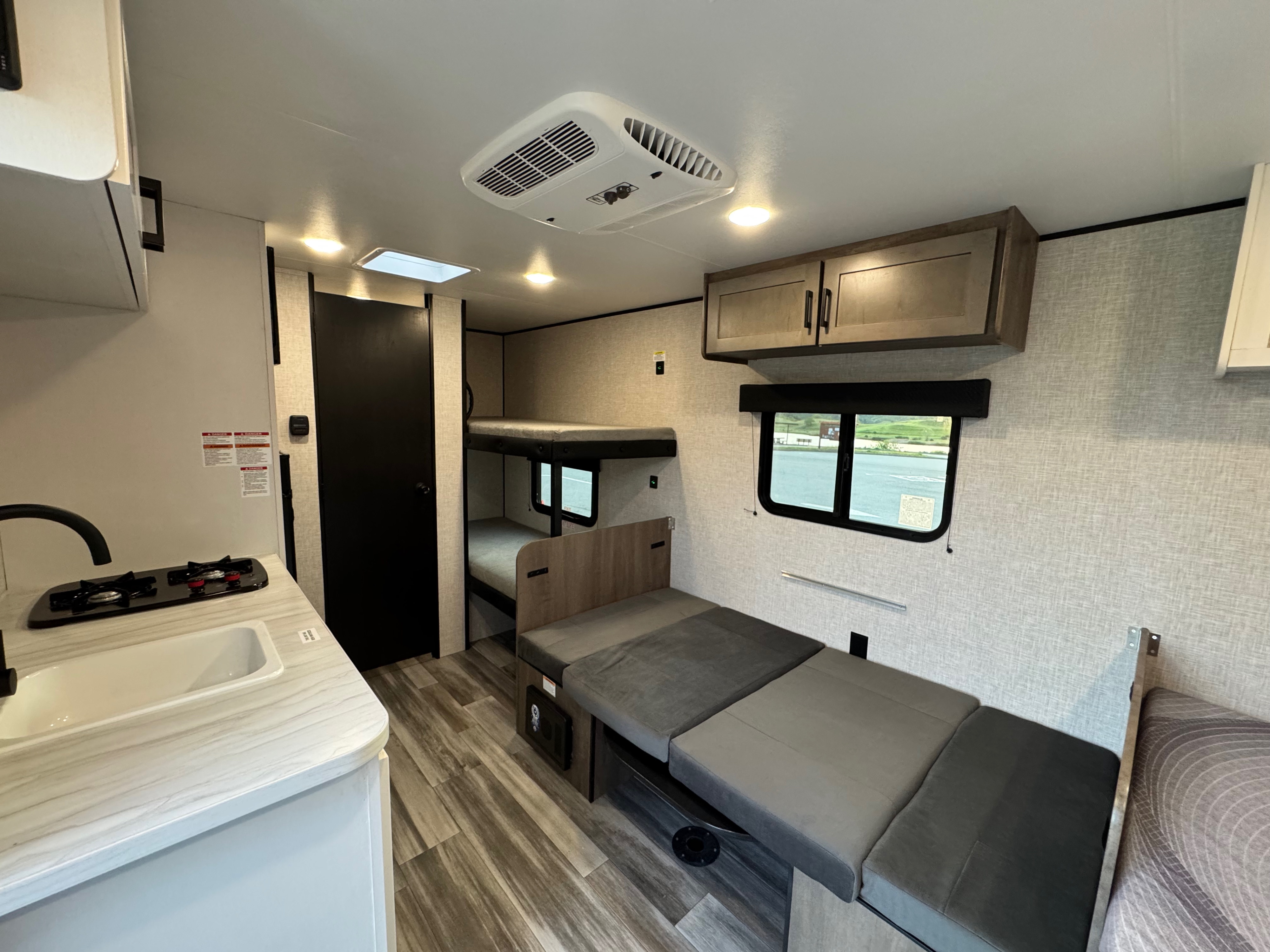 Inside an RV rental, showing the kitchen area, bunk beds, and versatile dinette/sofa. A compact, functional interior.. Jayco Jay Flight 2025