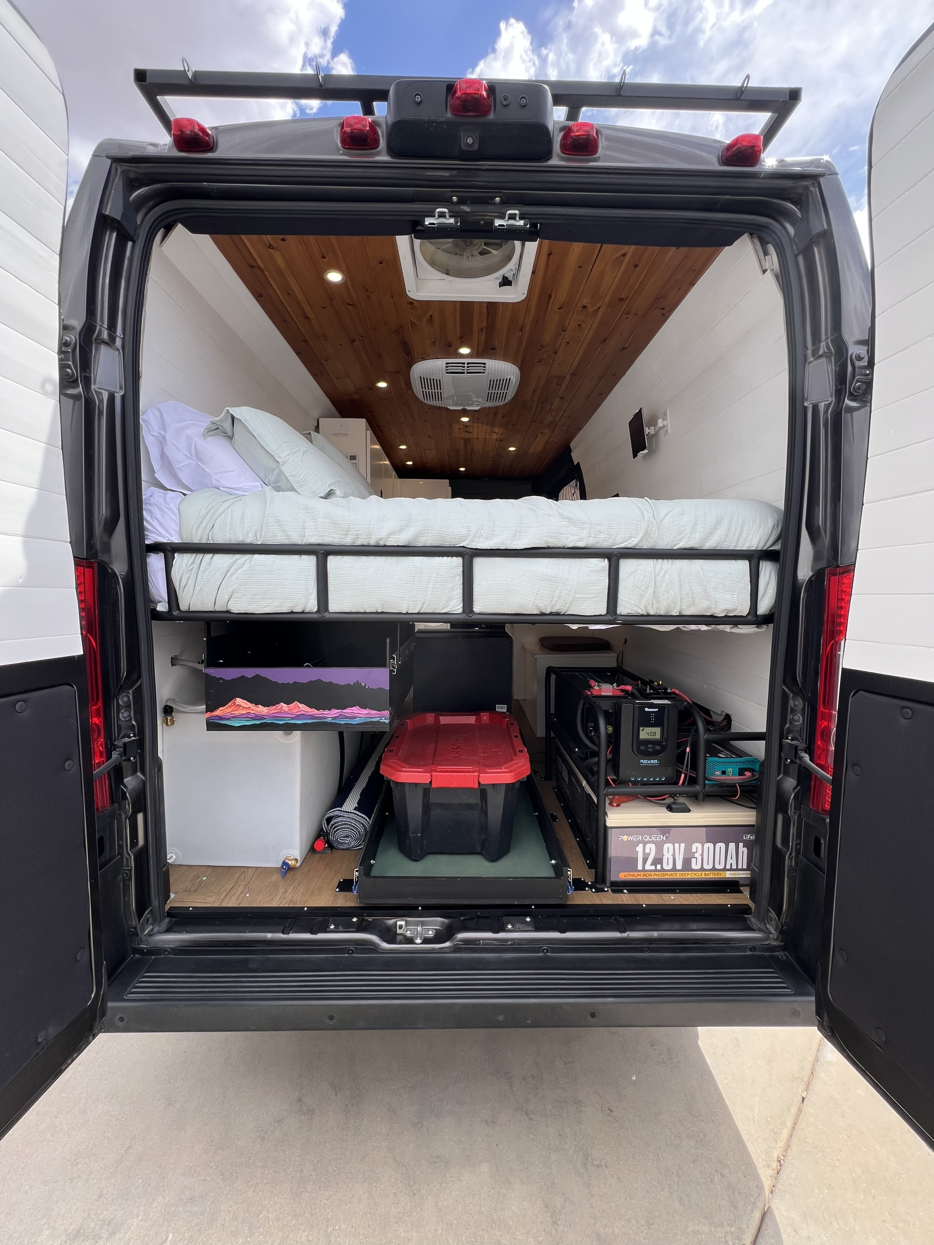 Rear view of an RV rental van's organized interior: elevated bed, slide-out storage, and a robust power station.. Dodge Ram Promaster 2500 2022