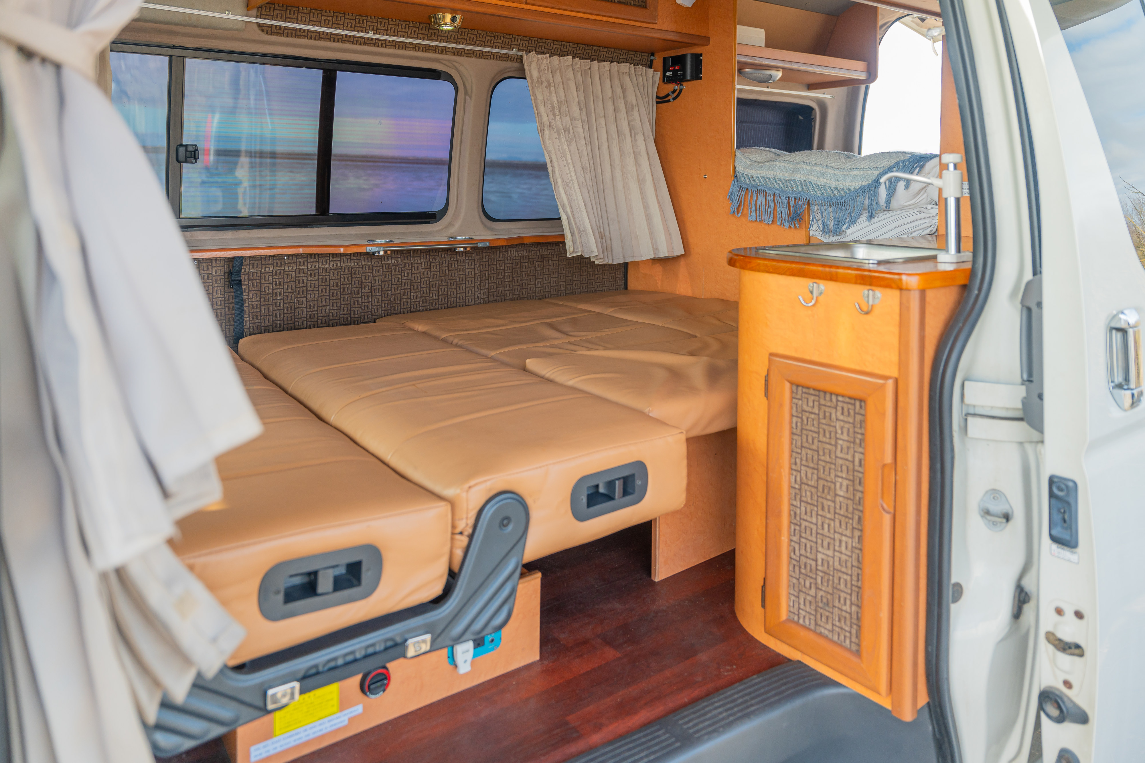 Cozy RV rental interior featuring a comfortable bed, windows with a view, and a compact kitchenette. Perfect for road trips!. Toyota Hiace 2007