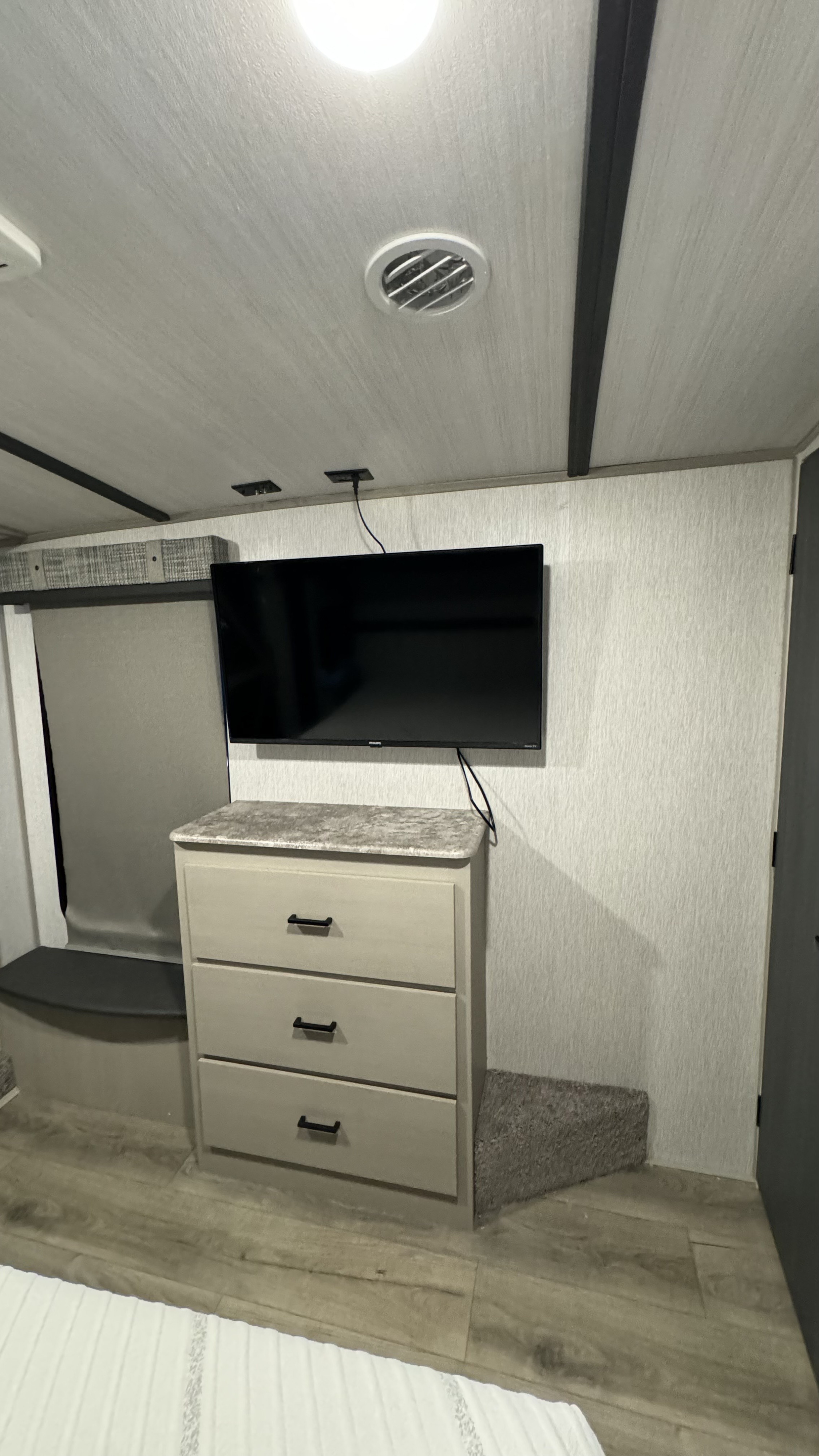 This RV rental bedroom features a wall-mounted TV above a three-drawer dresser and compact window seating, maximizing space.. Forest River Salem Hemisphere 2023