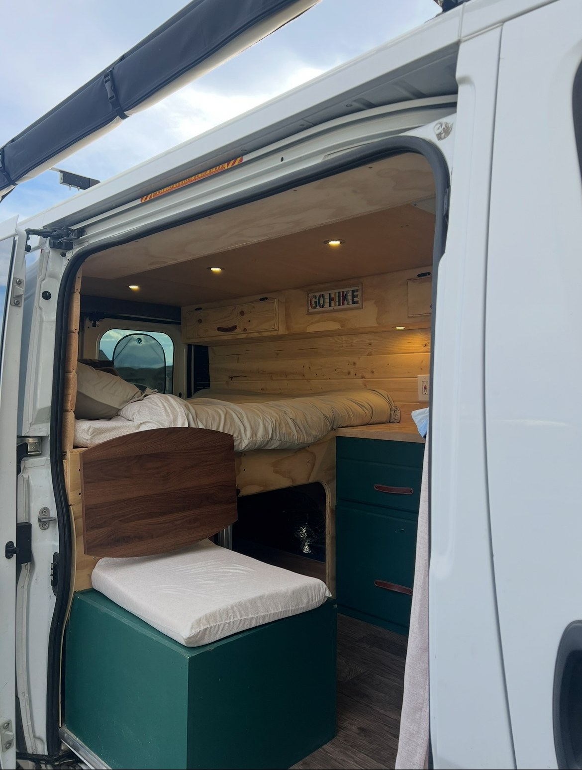 Inside a custom rv rental camper van, featuring a cozy bed, seat, and teal cabinets with wood accents for your next adventure.. RAM Promaster 2017