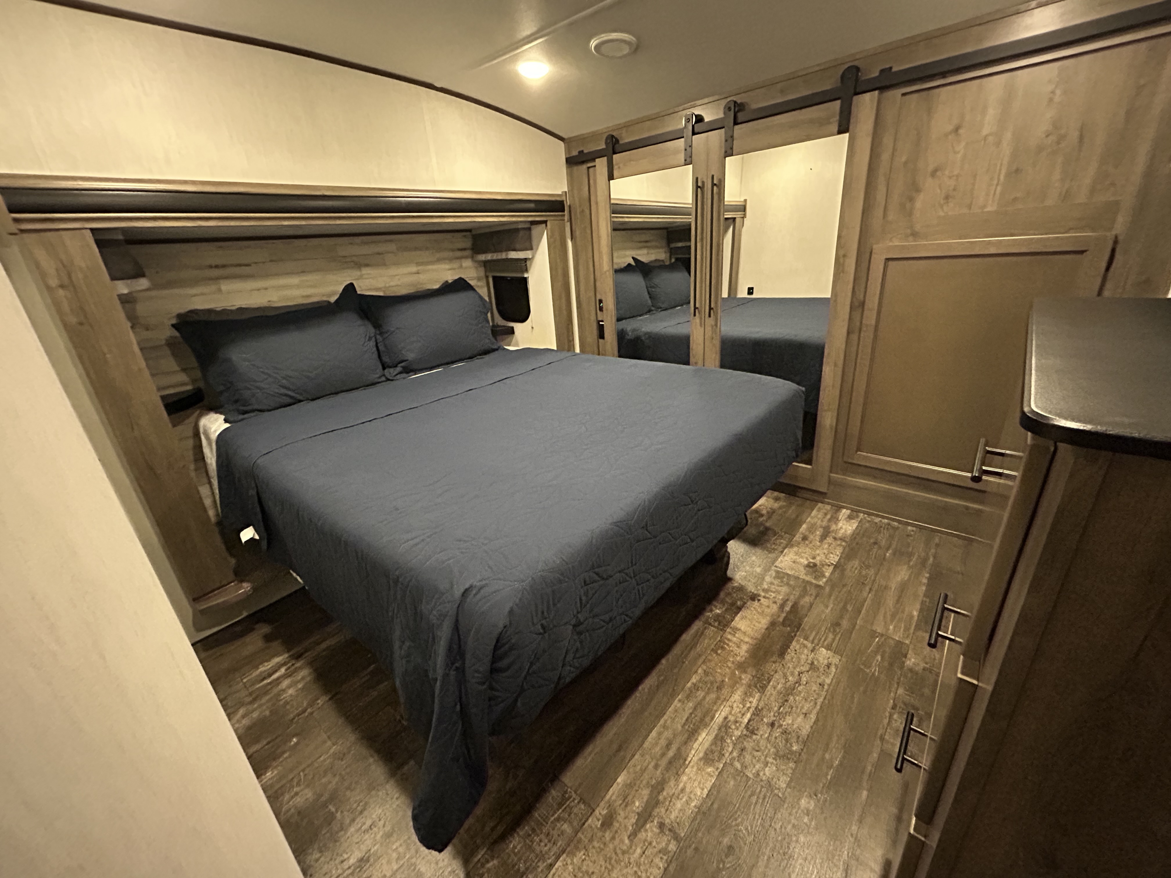 RV rental bedroom: dark blue bed, wood headboard, mirrored sliding barn doors, and wood-look floor.. Forest River Sabre 2022