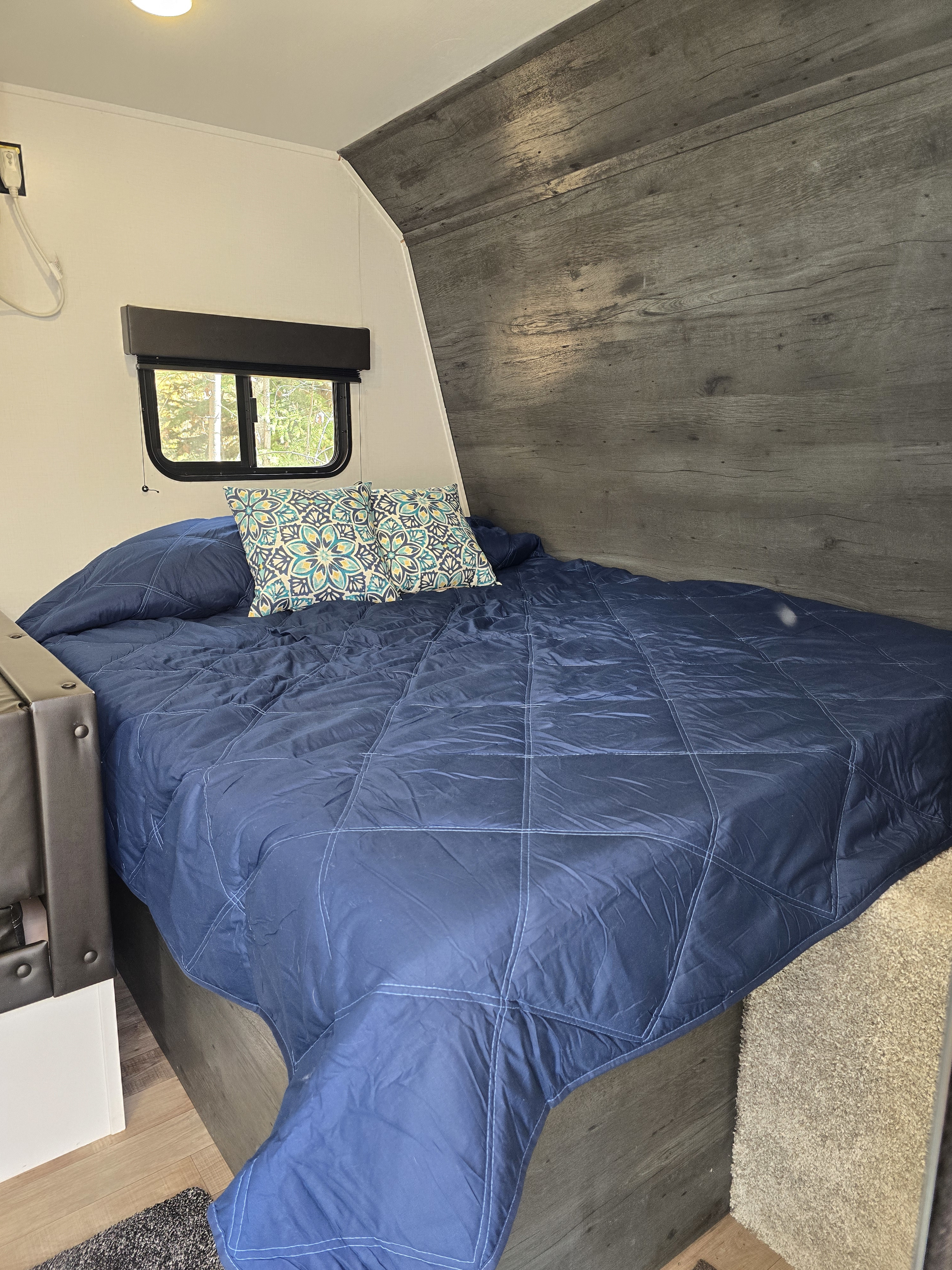 Inside an RV rental: a cozy bedroom featuring a comfortable bed with navy blue bedding and a window overlooking nature.. Keystone RV Hideout 2022