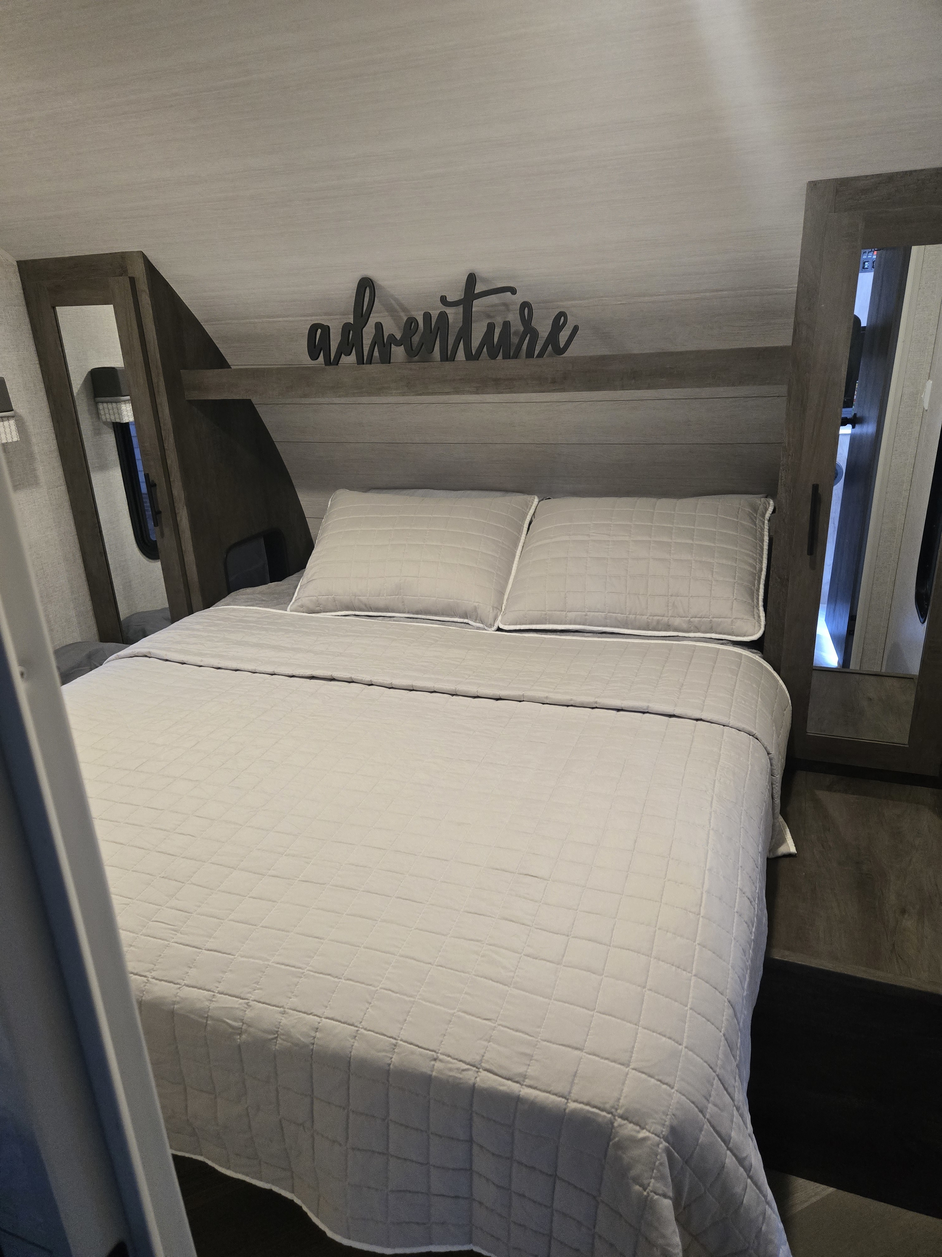 Comfortable RV rental bedroom featuring a clean bed, overhead shelf with an "adventure" sign, and bedside mirrors.. Forest River Salem Cruise Lite 2021