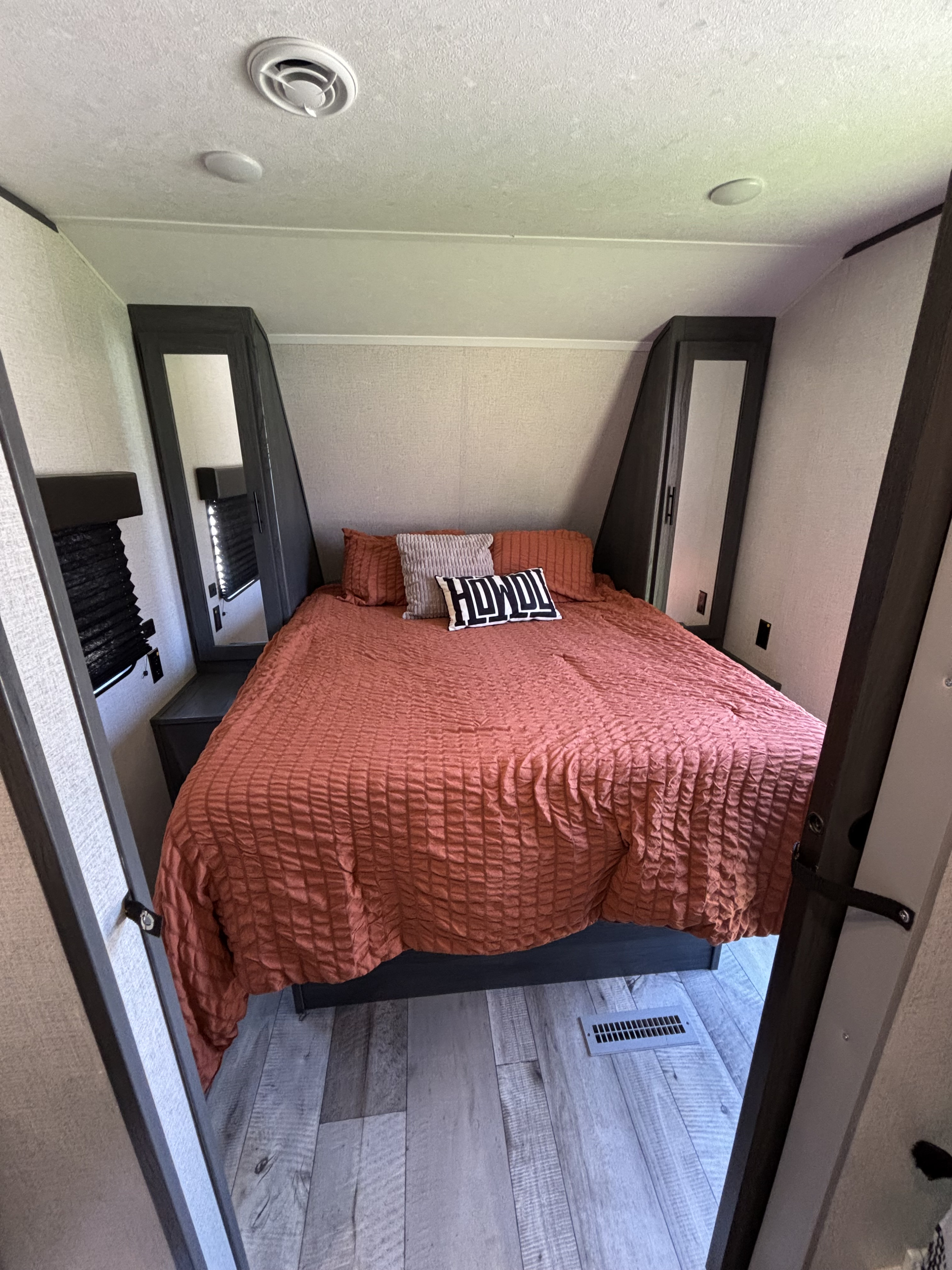 Cozy RV rental bedroom featuring a large bed with rust-colored bedding, built-in storage, and wood-look flooring.. Aspen Trail LE 2022