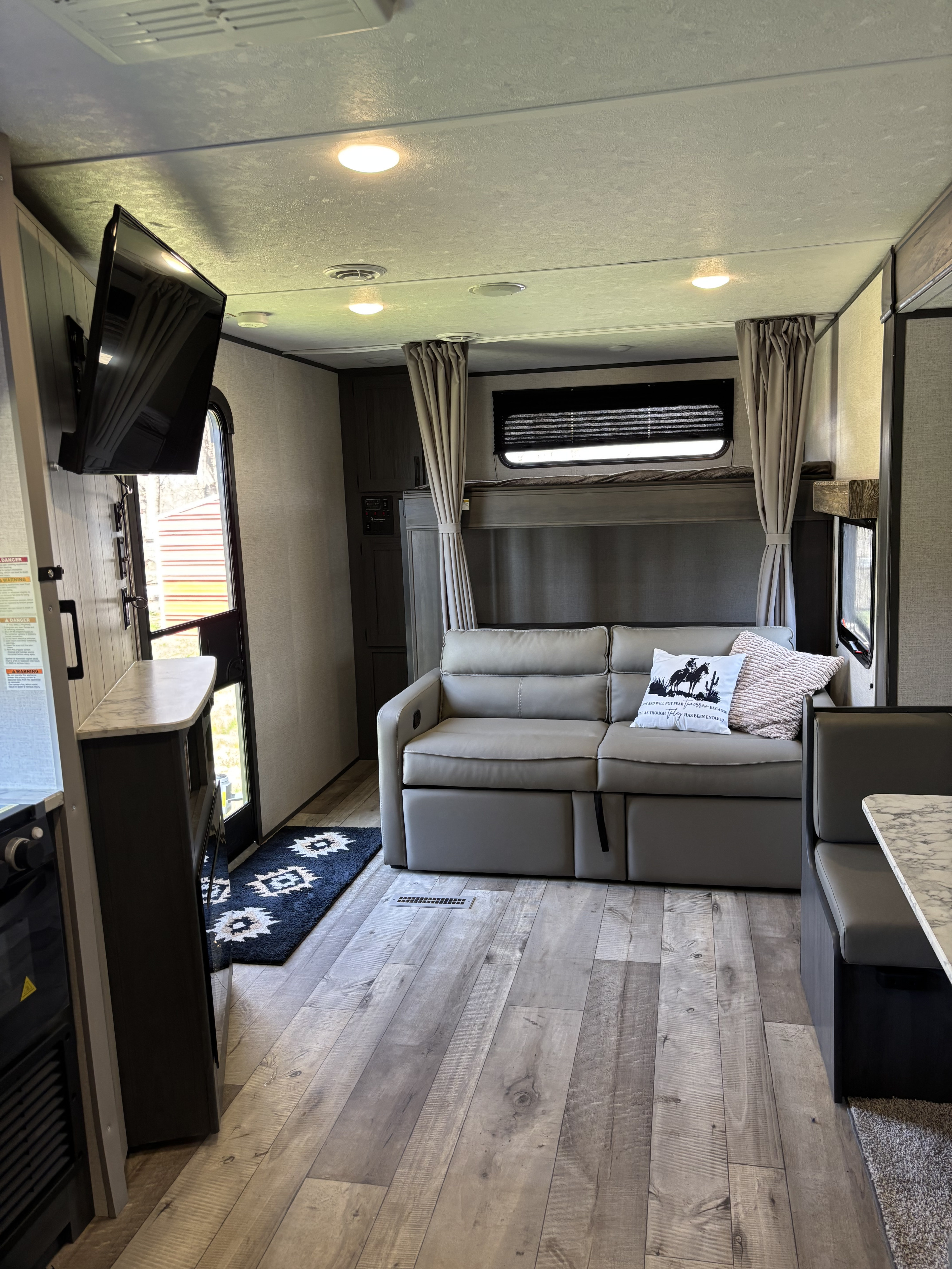 Spacious RV rental interior featuring a comfy sofa, bunk beds, TV, and dining booth, ready for travel.. Aspen Trail LE 2022