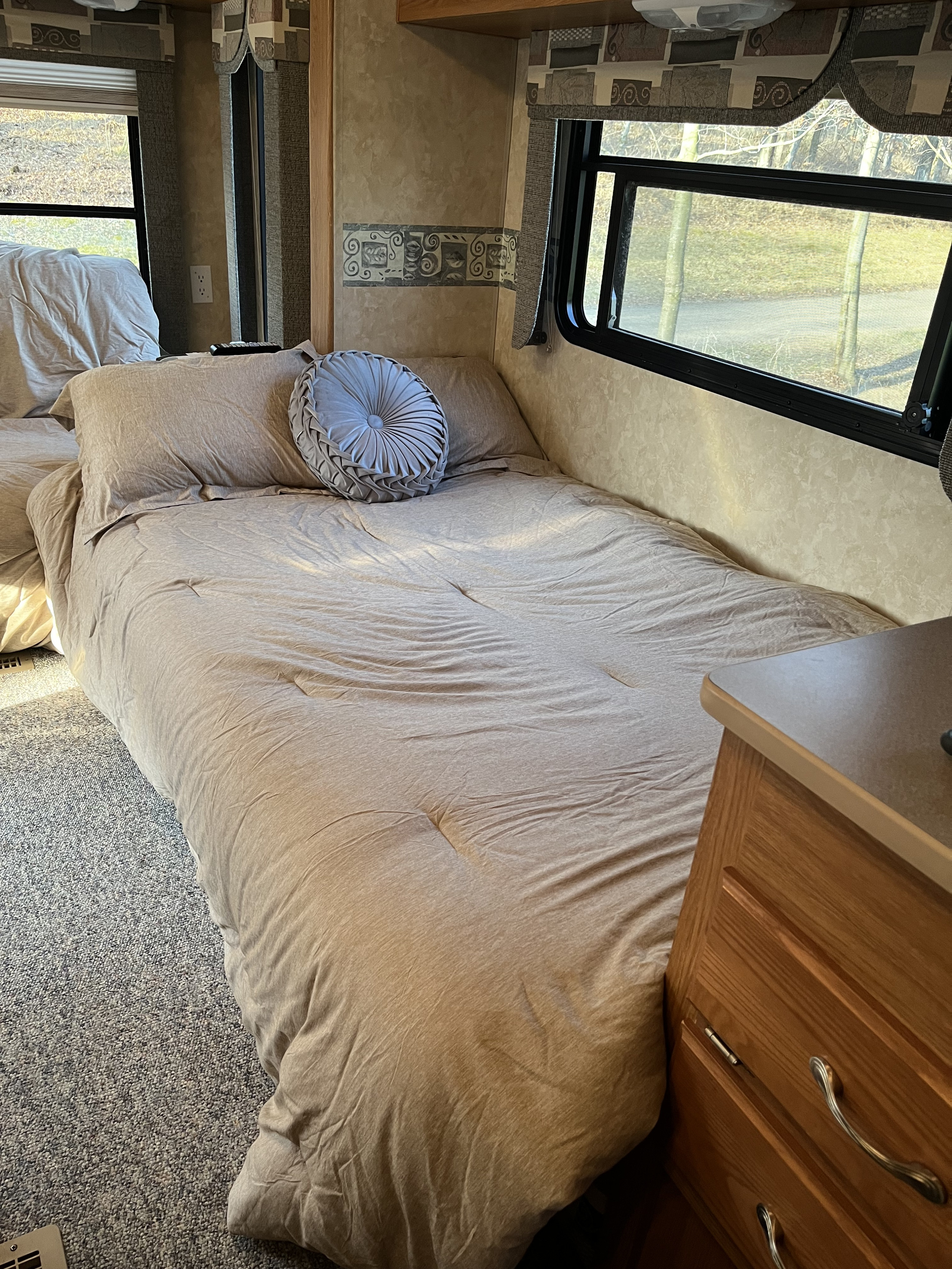 An RV rental bedroom featuring a comfy bed with soft bedding & a decorative pillow, windows, and wood nightstand.. Frontier RV 2901 2008