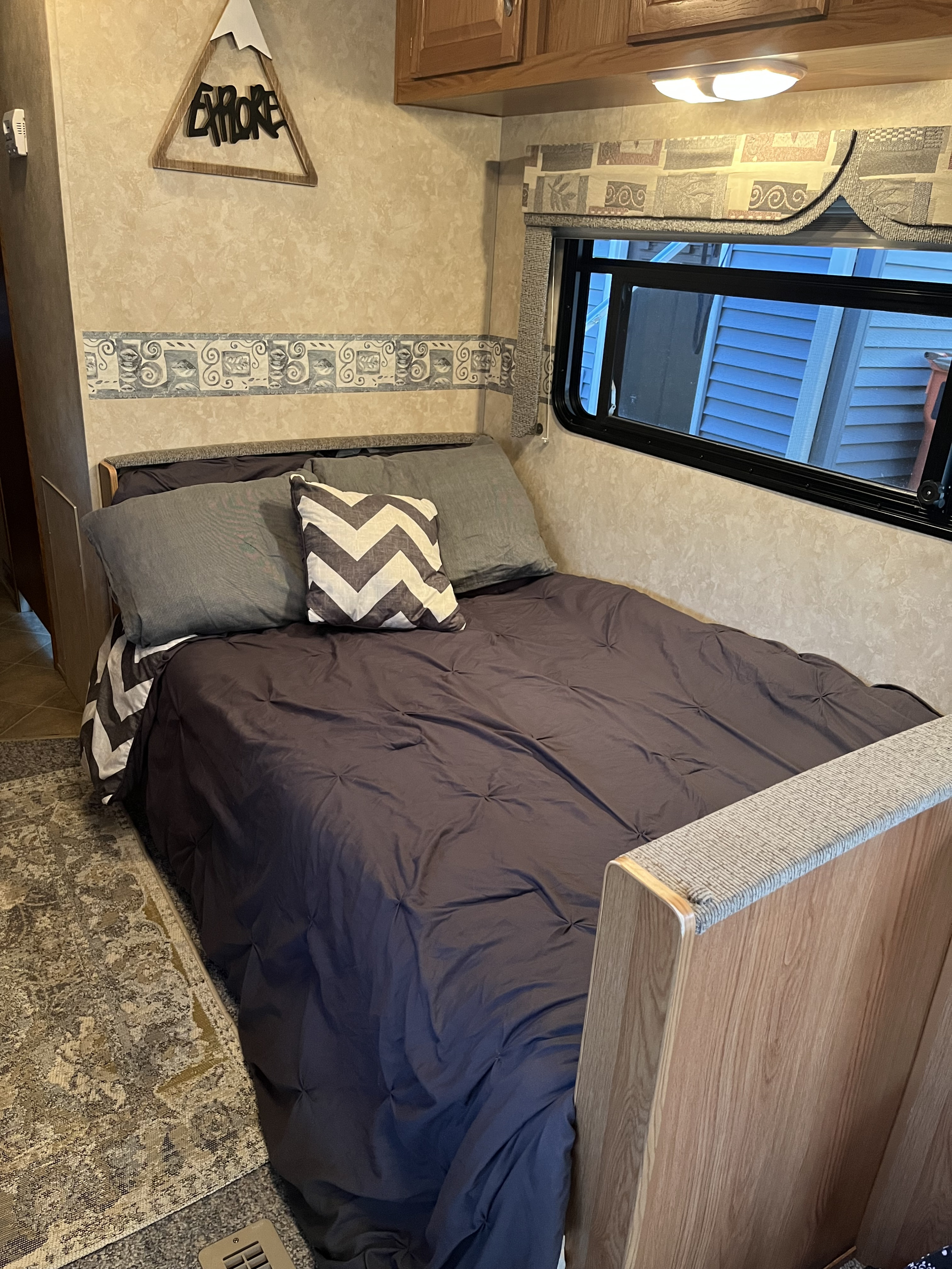 Cozy bedroom in an RV rental, showing a dark-quilted bed with chevron pillows, plus a mountain-shaped "EXPLORE" wall decor.. Frontier RV 2901 2008
